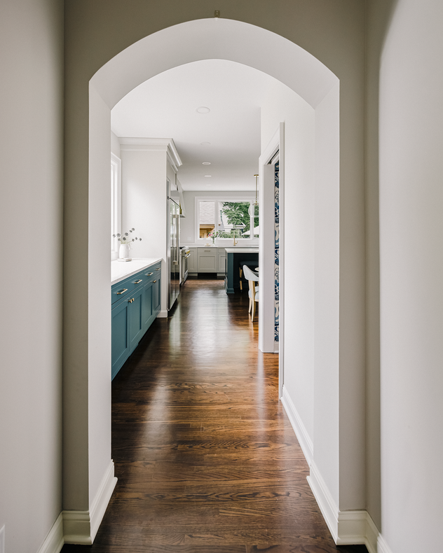 Archway leading to a kitchen with dark wooden floors, white walls, and blue cabinets.