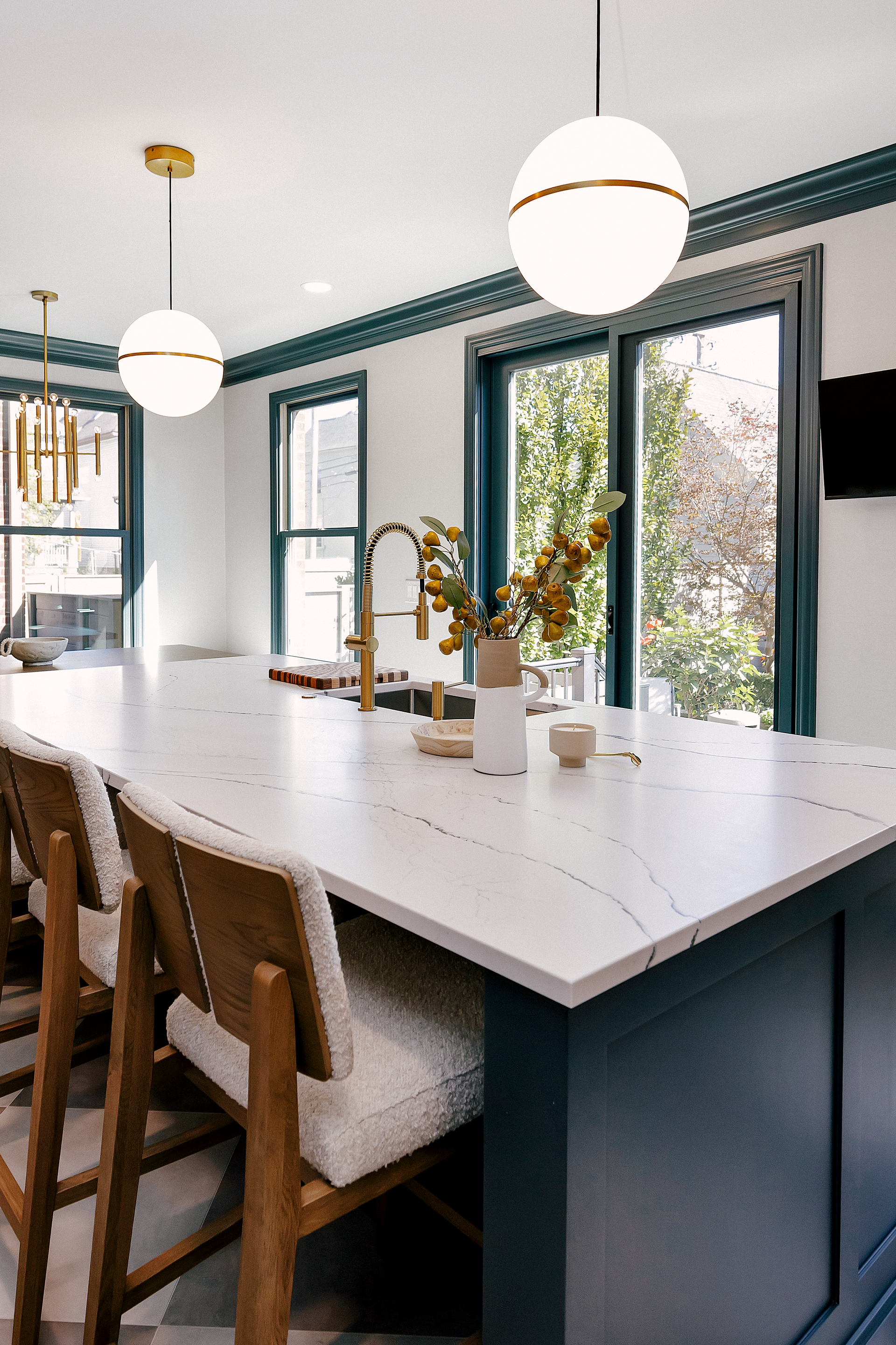 Kitchen with white countertop island, pendant lights, and bar stools. Teal trim, windows, and decorative items.
