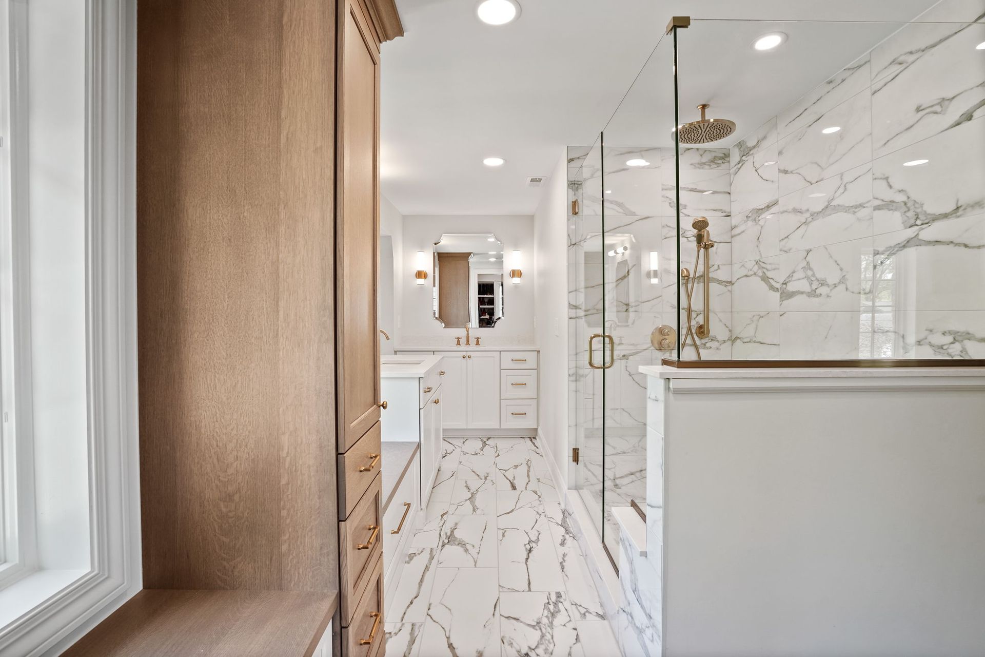 Bathroom with marble tile, glass shower, and wood vanity.