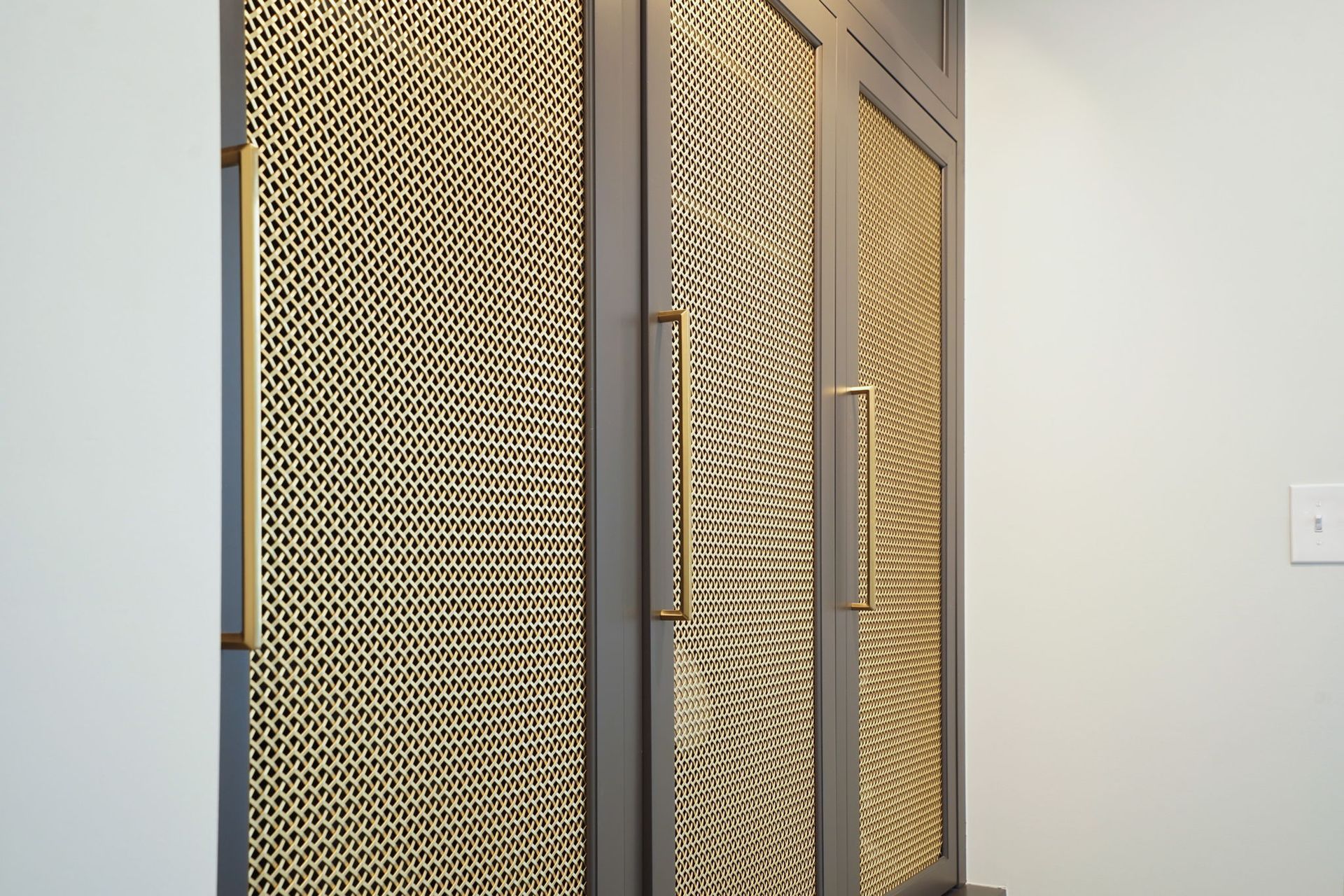Gray cabinet doors with gold mesh inserts and gold handles against a light blue wall.