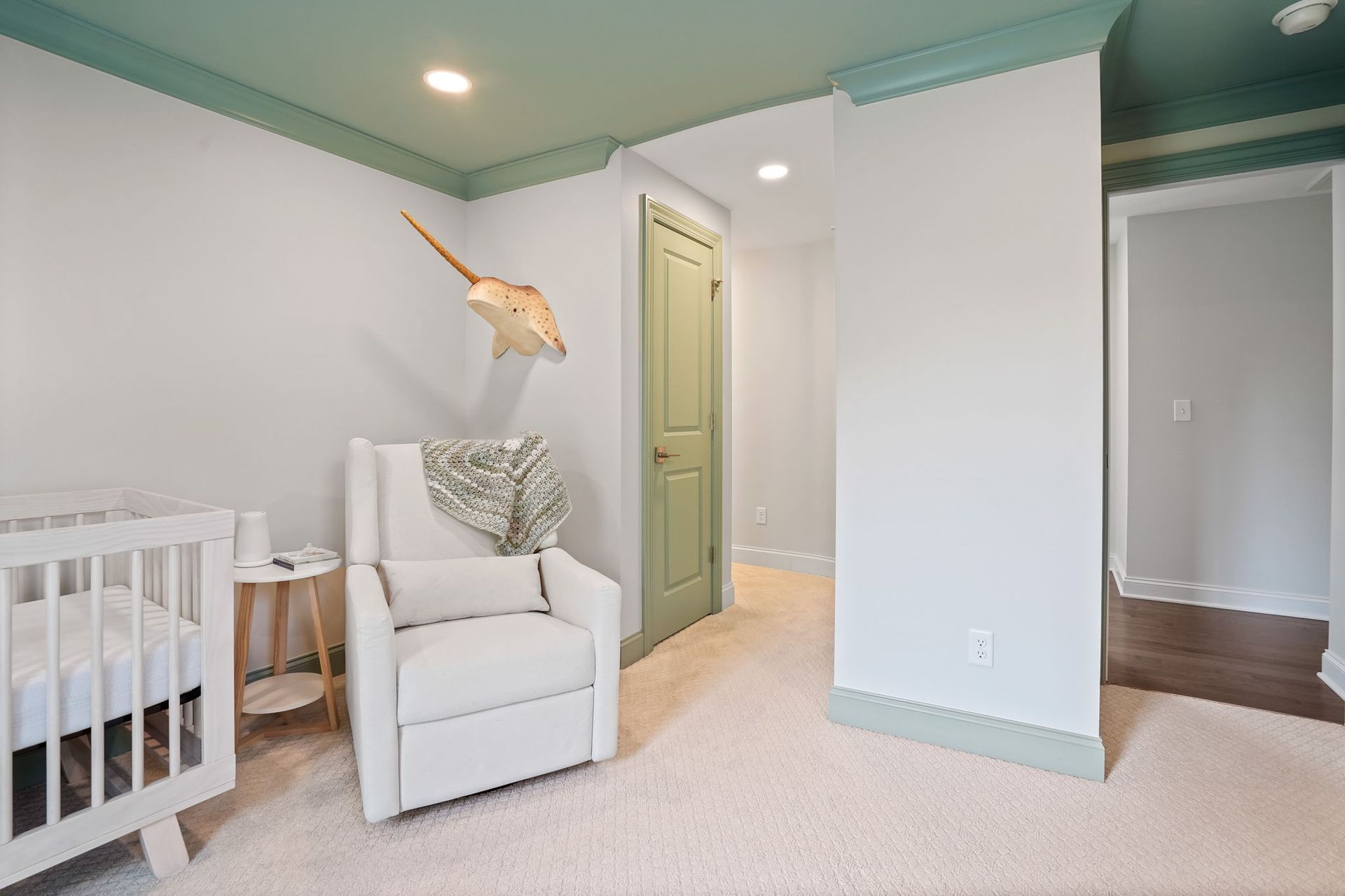 Nursery with white walls, green trim and door, white crib, armchair, and stingray art.