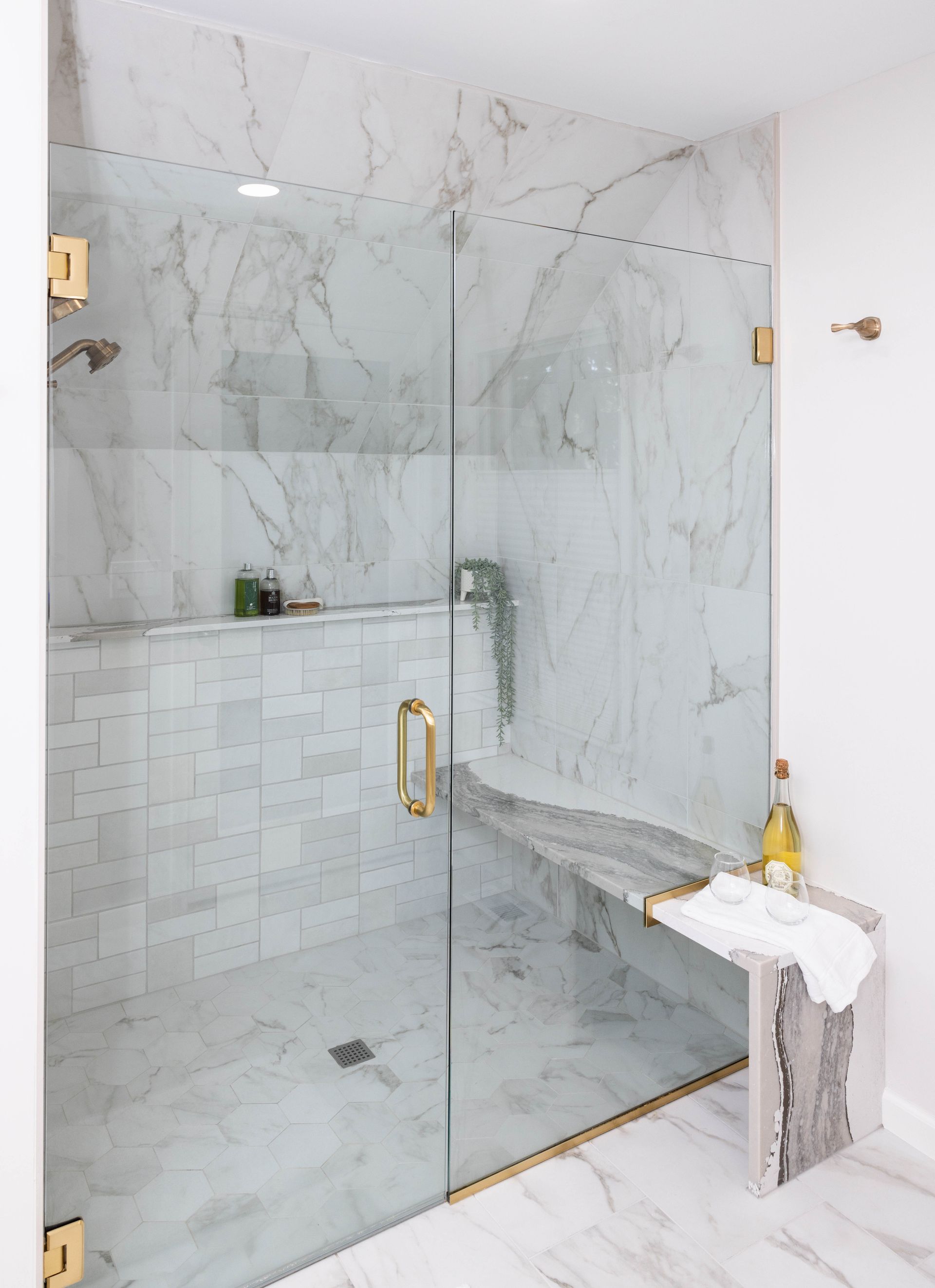 Luxurious shower with marble walls, glass door, and stone bench, with gold hardware.