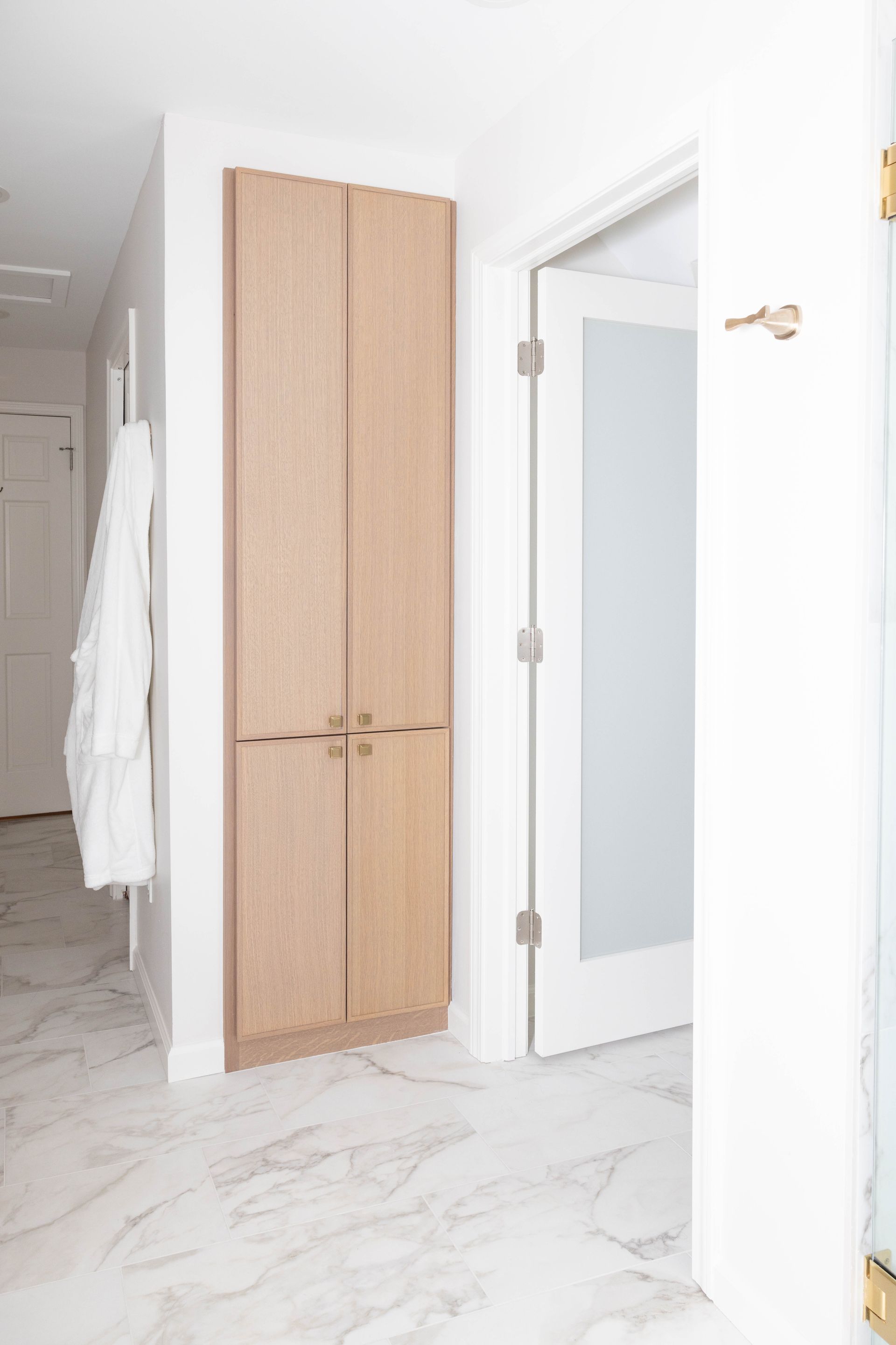 Tall light wood cabinet in a hallway next to an open door with frosted glass.