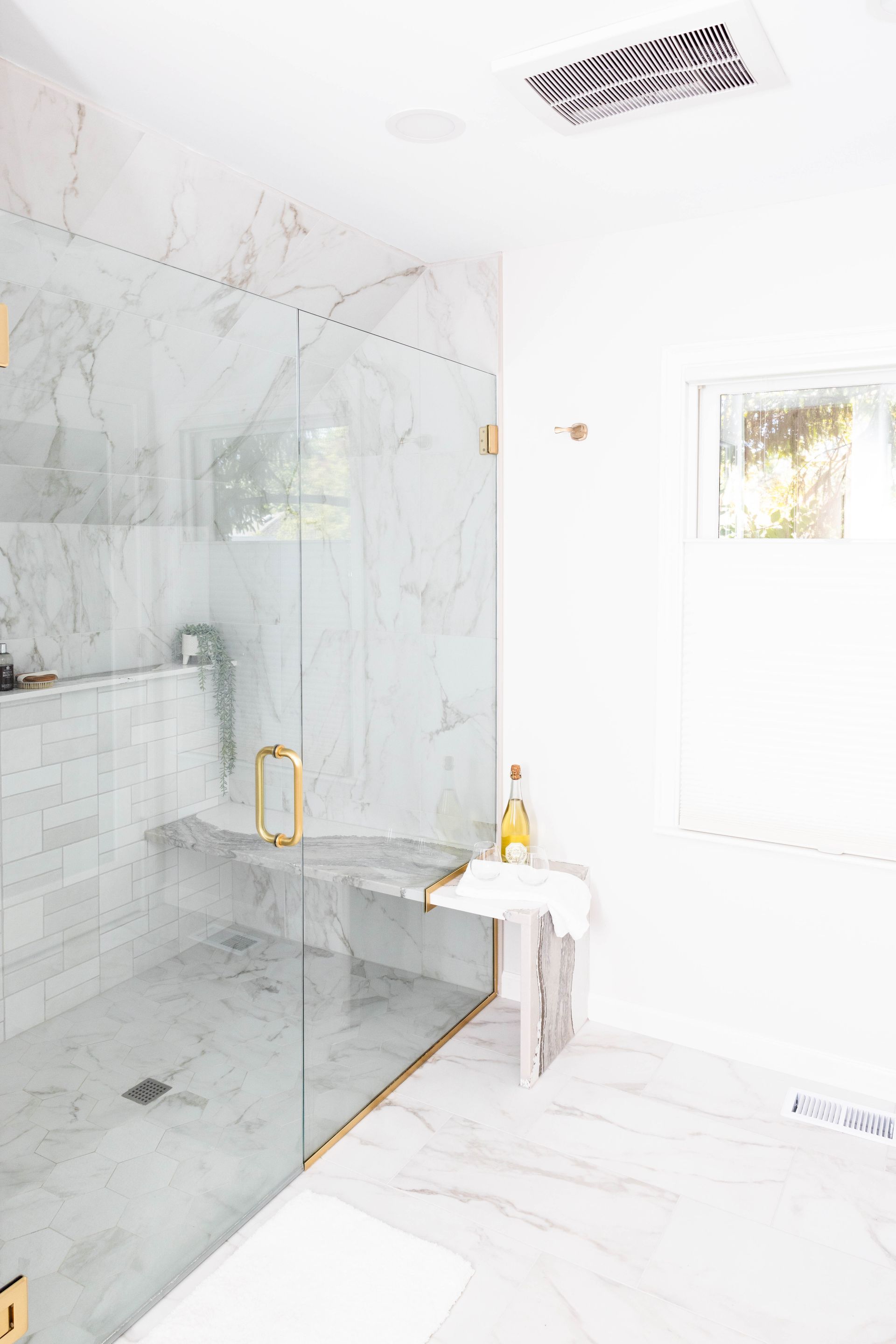 White marble bathroom with glass shower, gold accents.