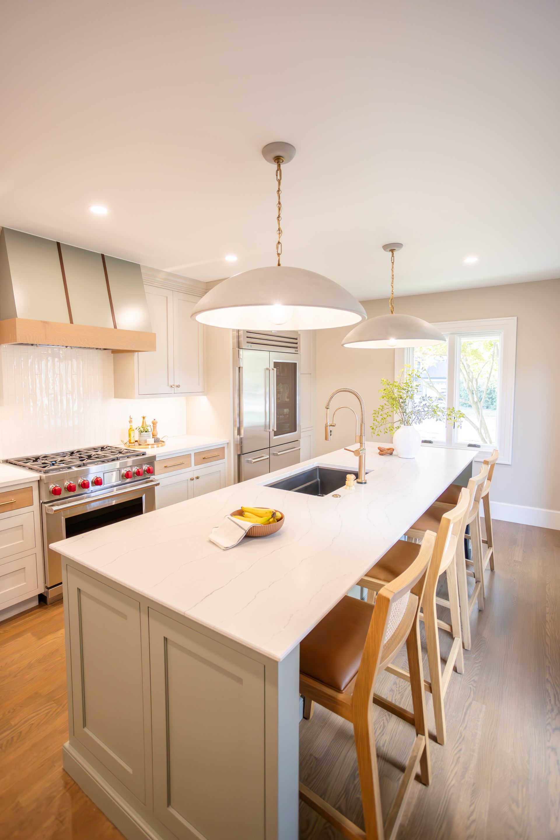 Kitchen with large island, pendant lights, wooden stools, and stainless steel appliances.