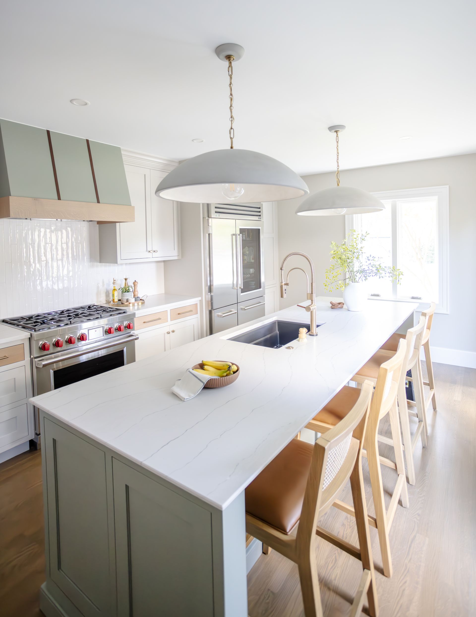Bright kitchen with island, pendant lights, and light blue cabinetry. Countertop with bar stools and a range.