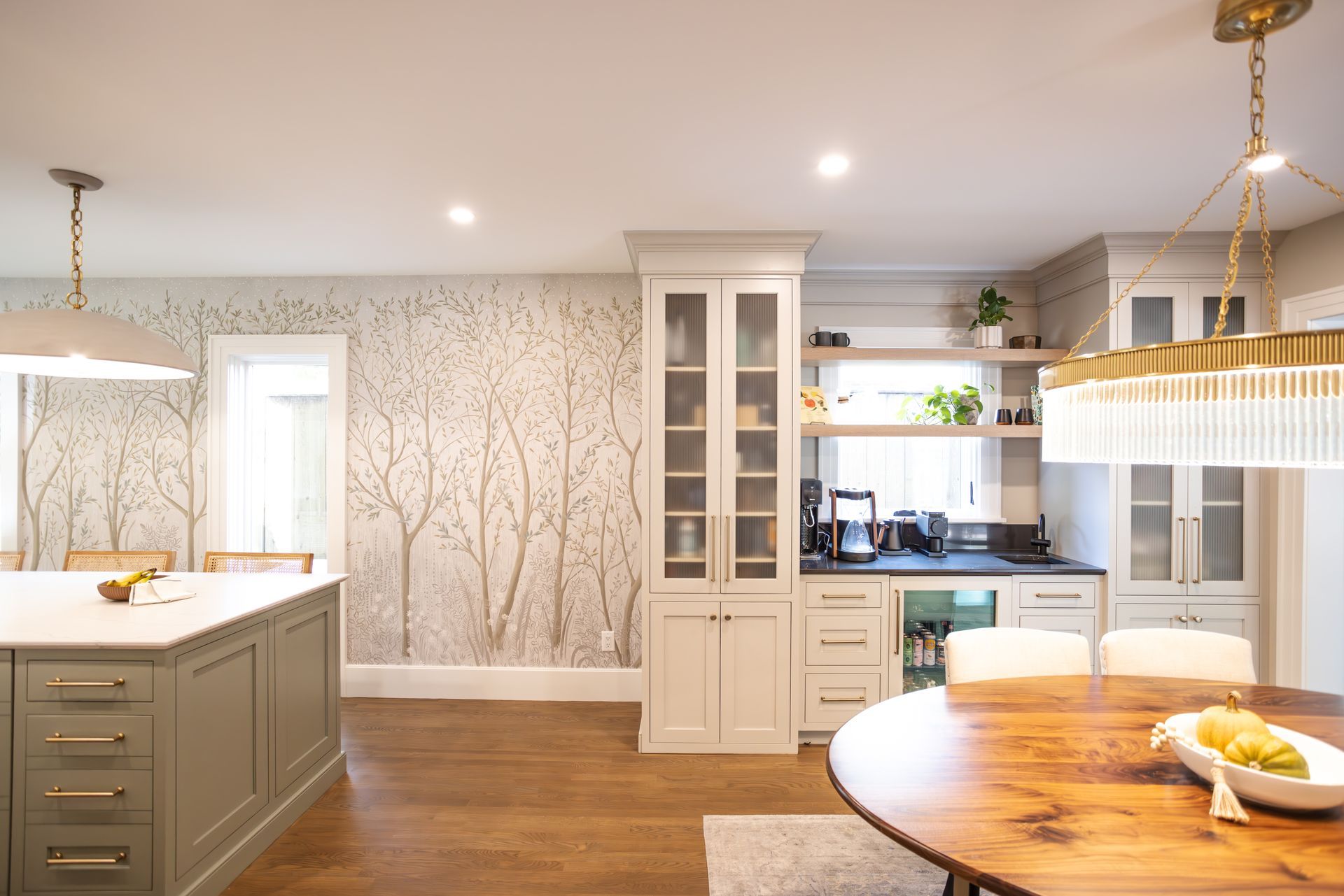 Modern kitchen with island, built-in cabinetry, wallpapered accent wall, and wooden dining table.