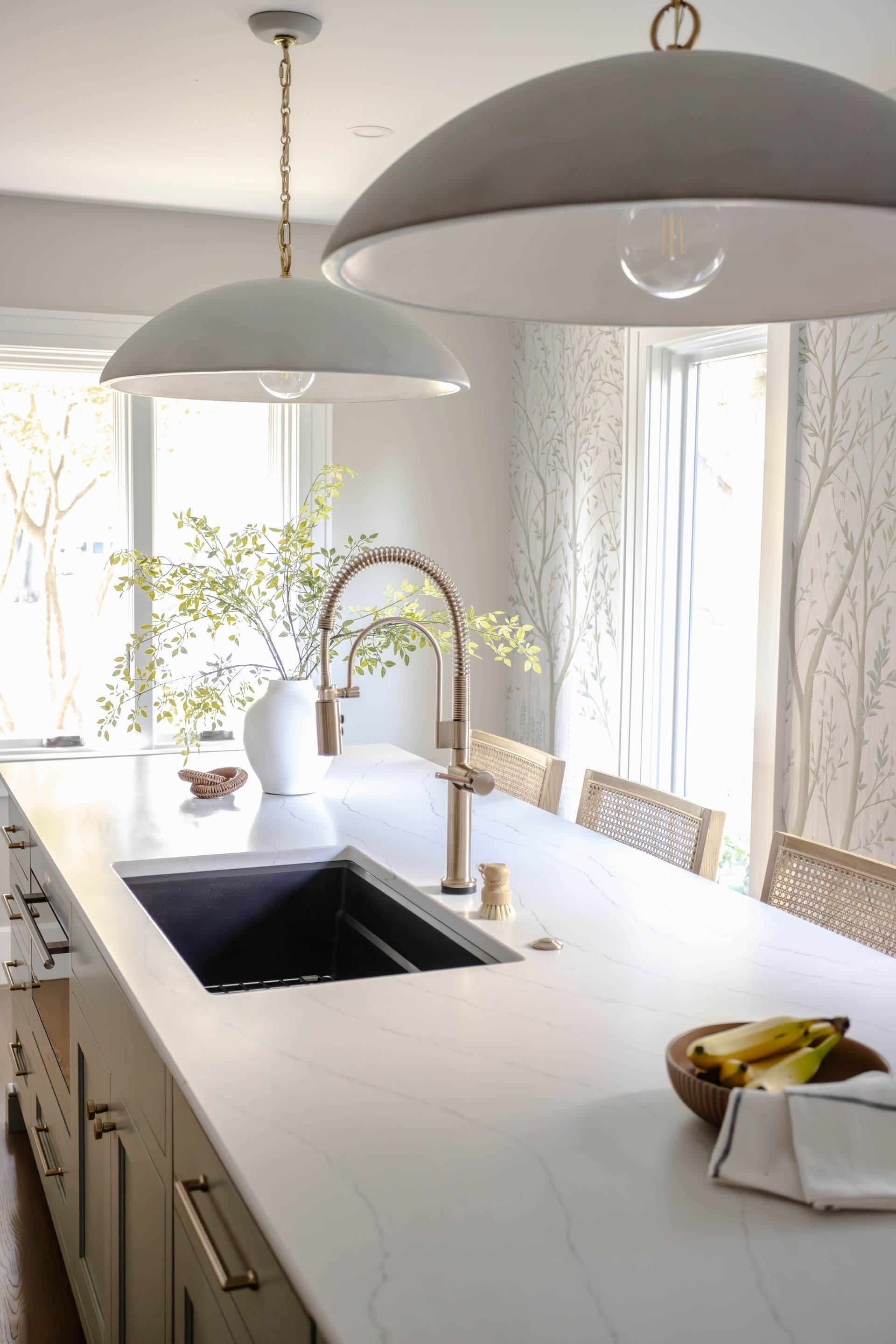 Modern kitchen island with sink, bronze faucet, white countertop, pendant lights, and decorative bowl with fruit.