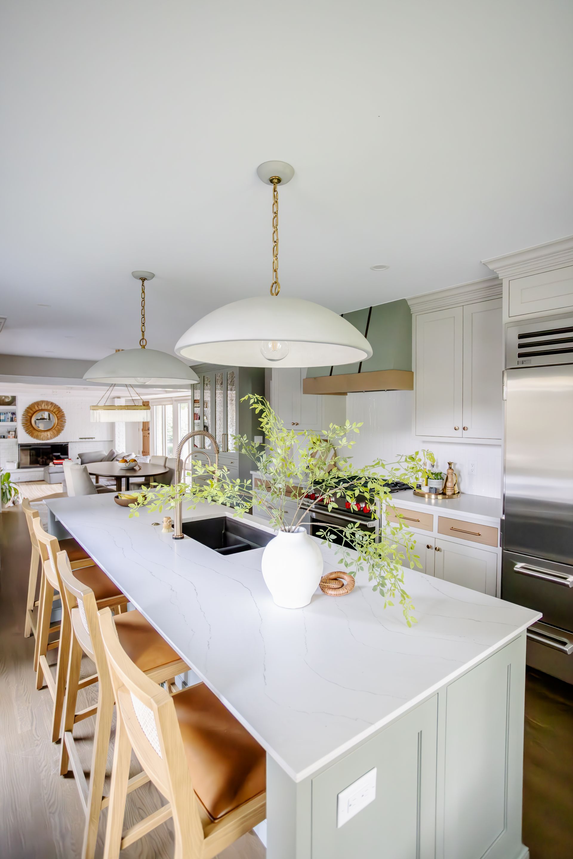 Spacious kitchen with a light green island, pendant lights, and bar stools.
