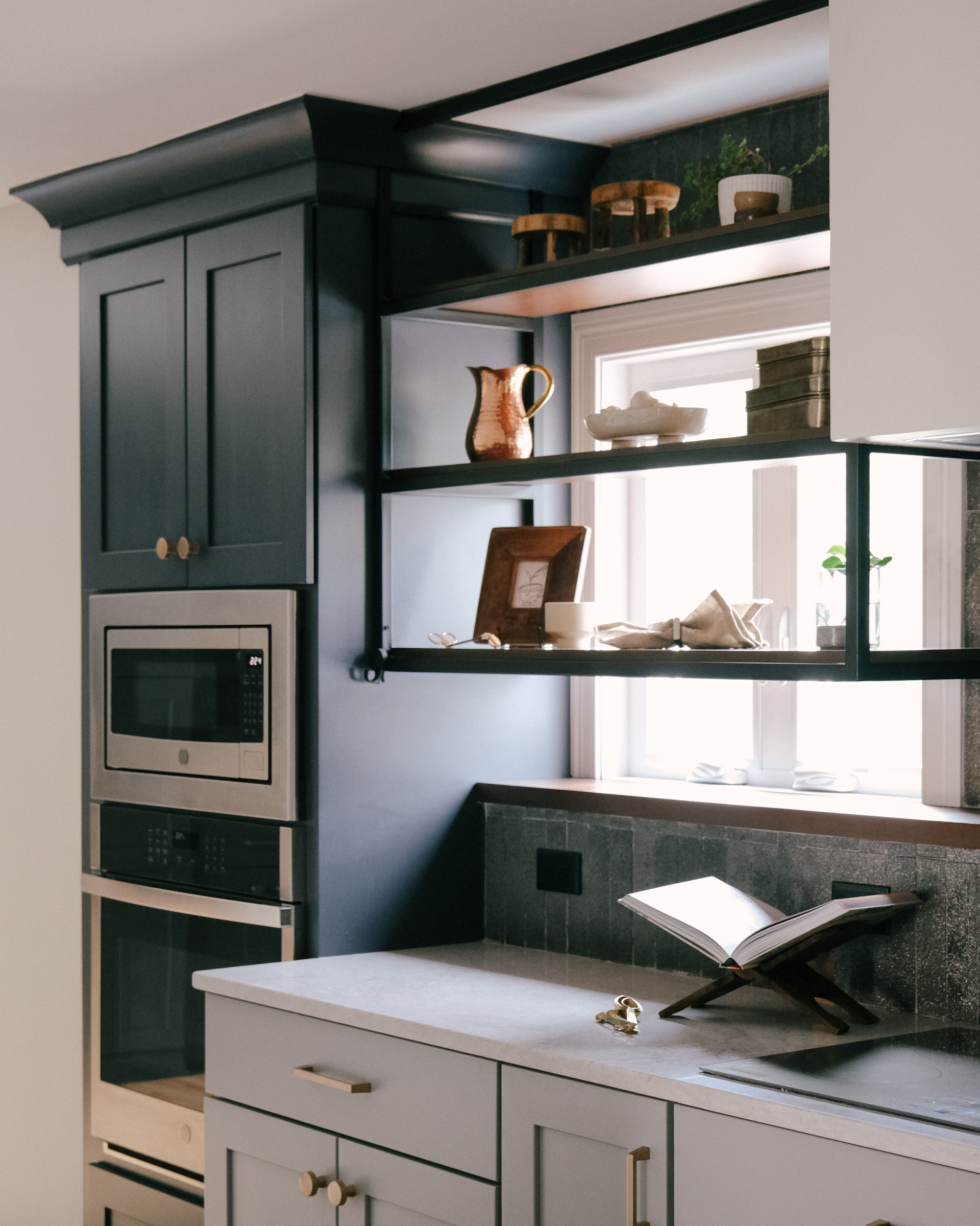 Kitchen with dark blue cabinets, open shelves, microwave, and a window. Light countertops and decor.