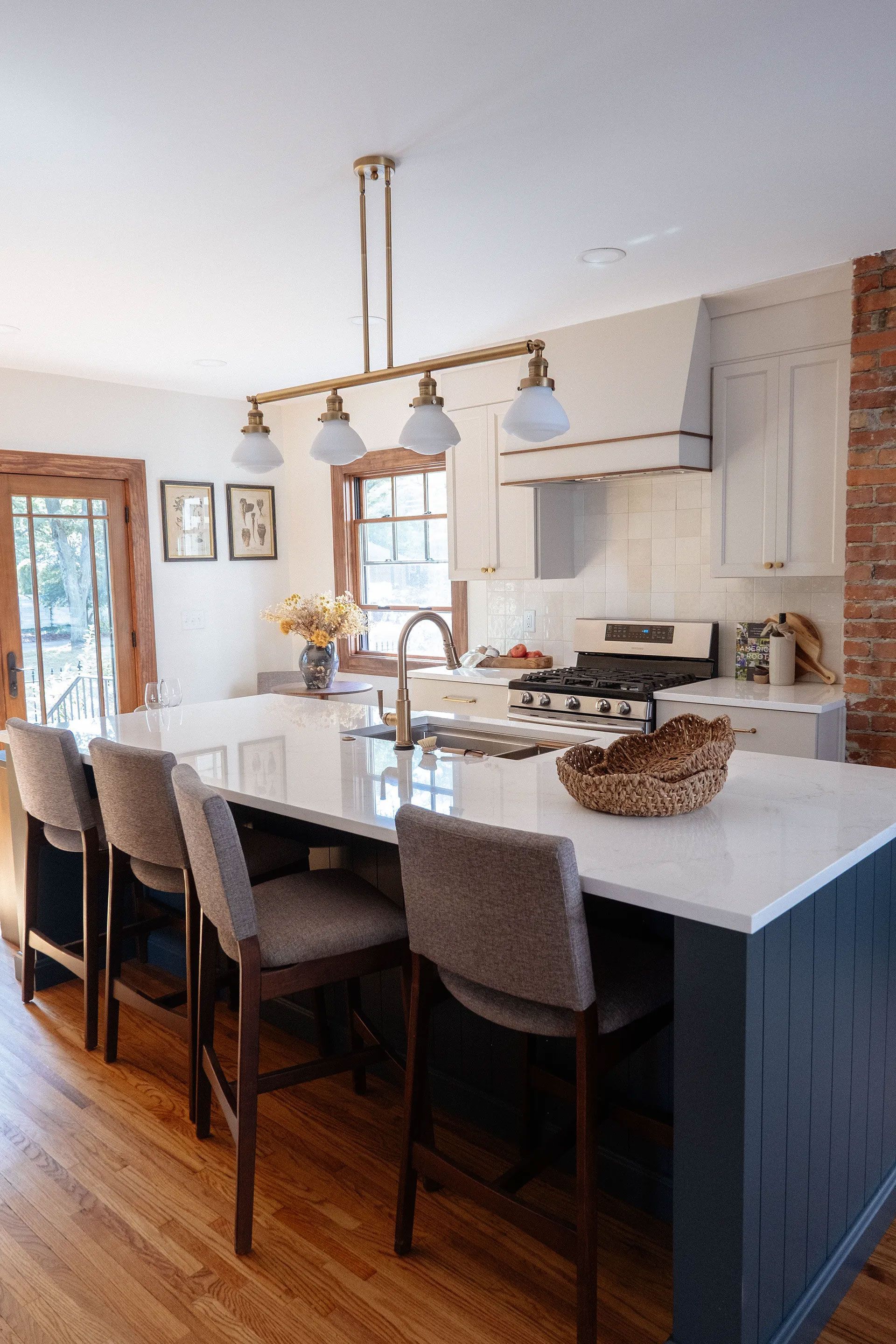 Kitchen with a dark blue island, white countertops, and gold light fixture. Chairs lined up at the island.