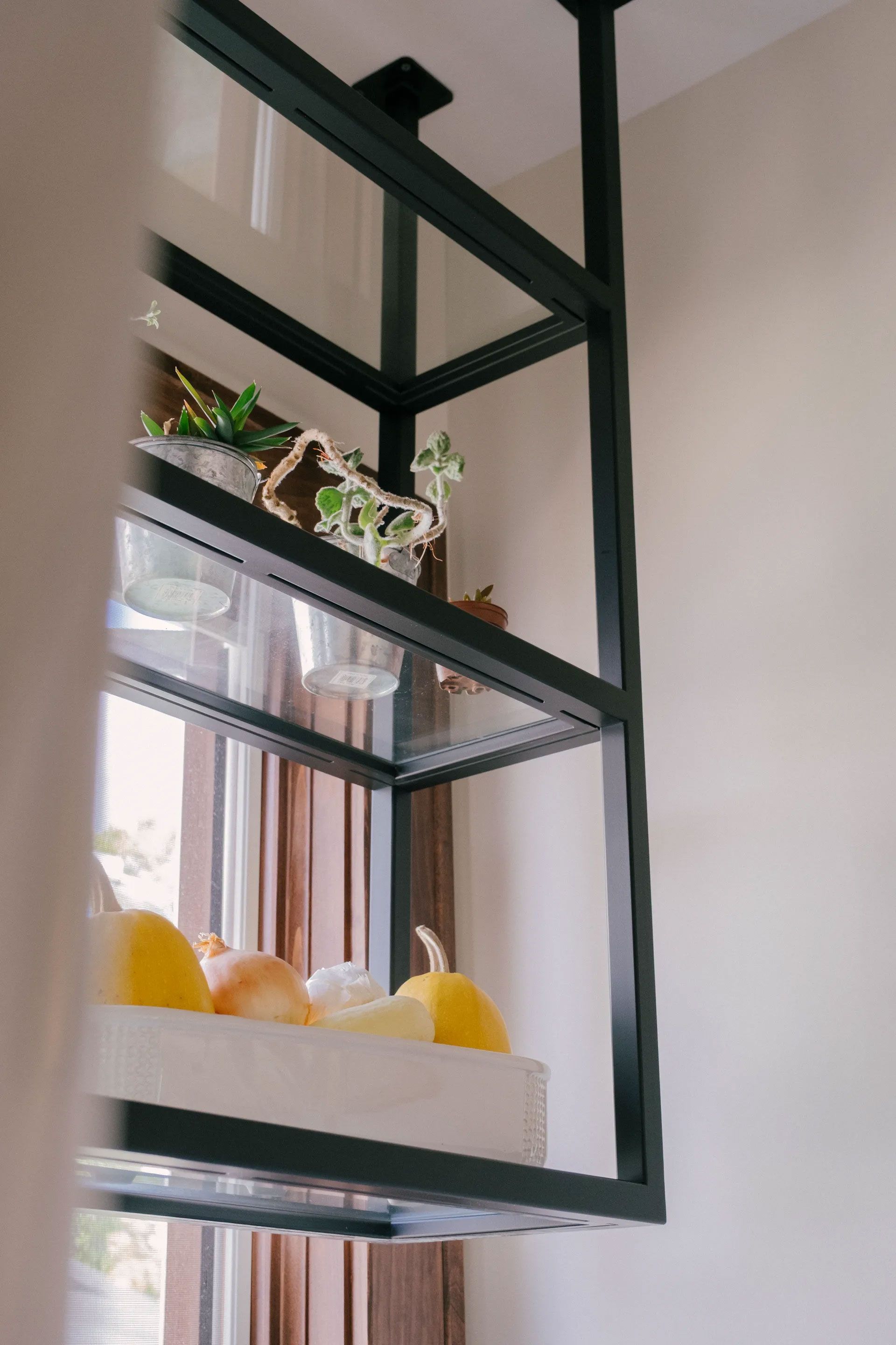 Black metal shelving unit hanging from the ceiling, holding decorative items and produce.
