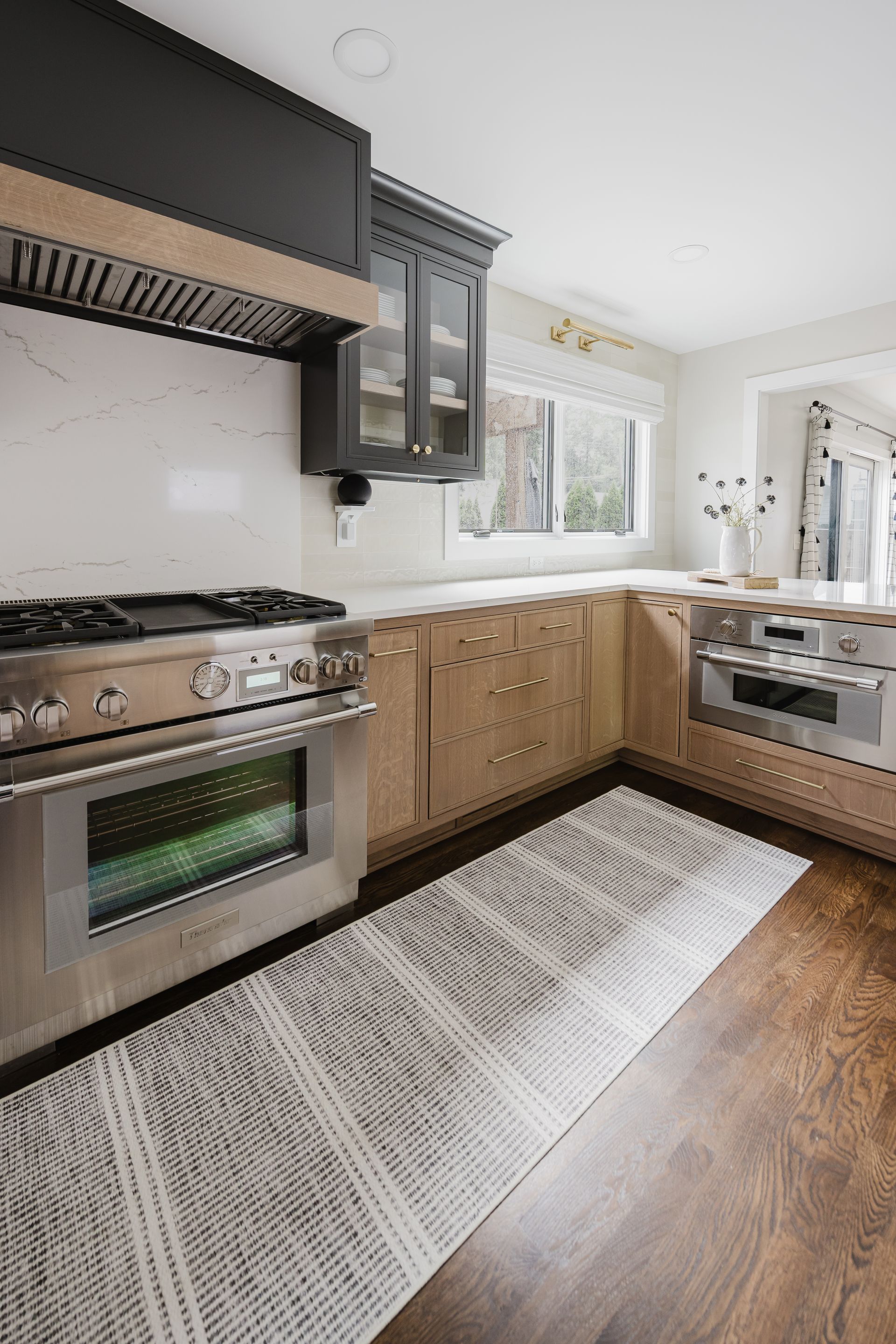 Modern kitchen with stainless steel appliances, light wood cabinets, and gray patterned rug.