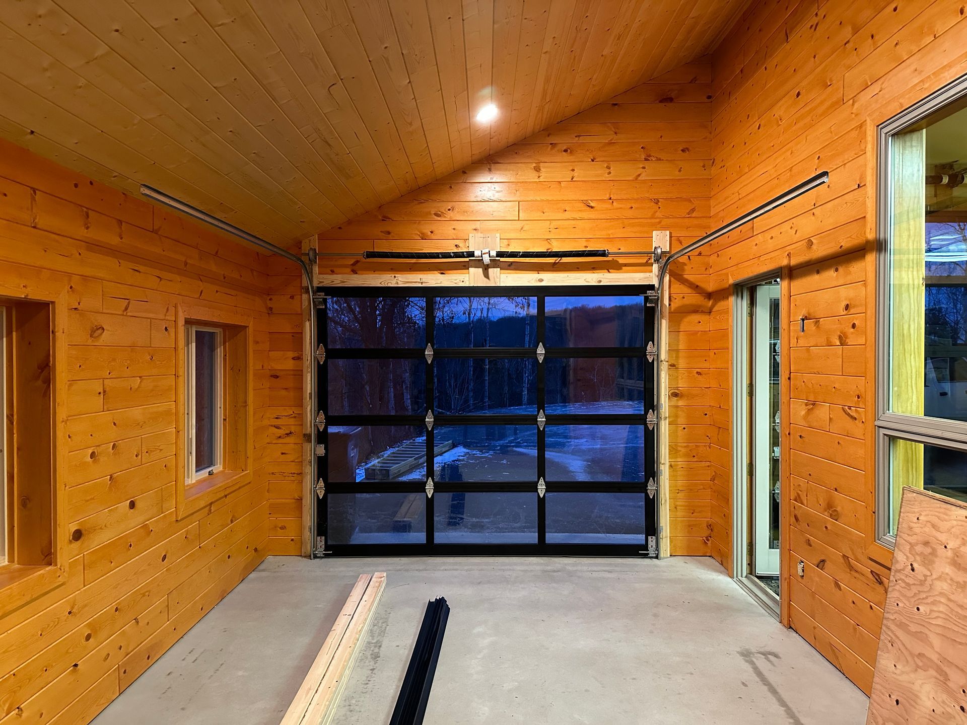 Interior of a garage with a glass door, light wood walls, and a concrete floor.