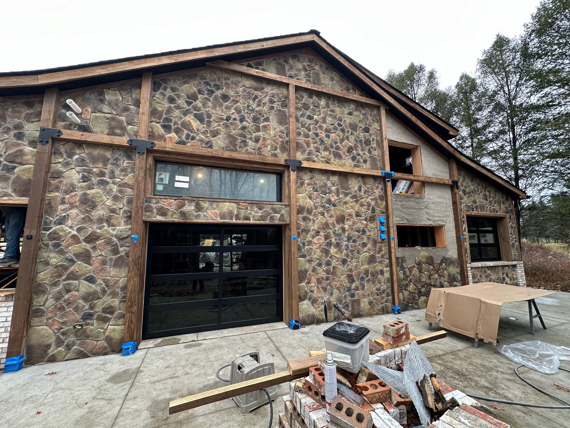 Stone building under construction with exposed wood framing, garage door, windows.