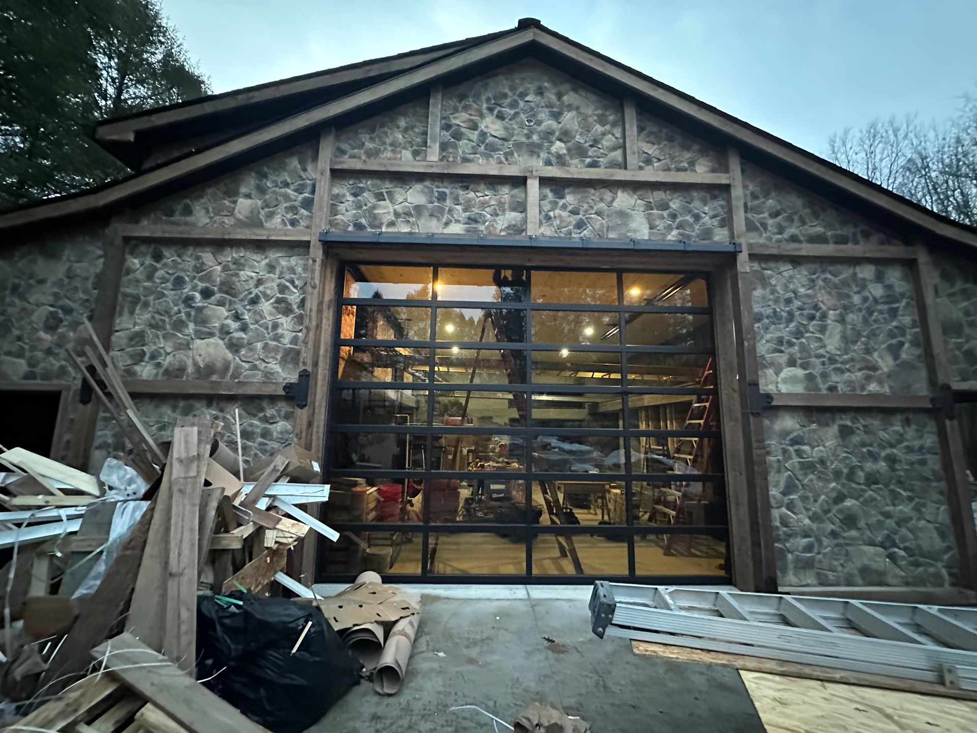 Stone building with a large glass garage door, a pile of wood debris in front.