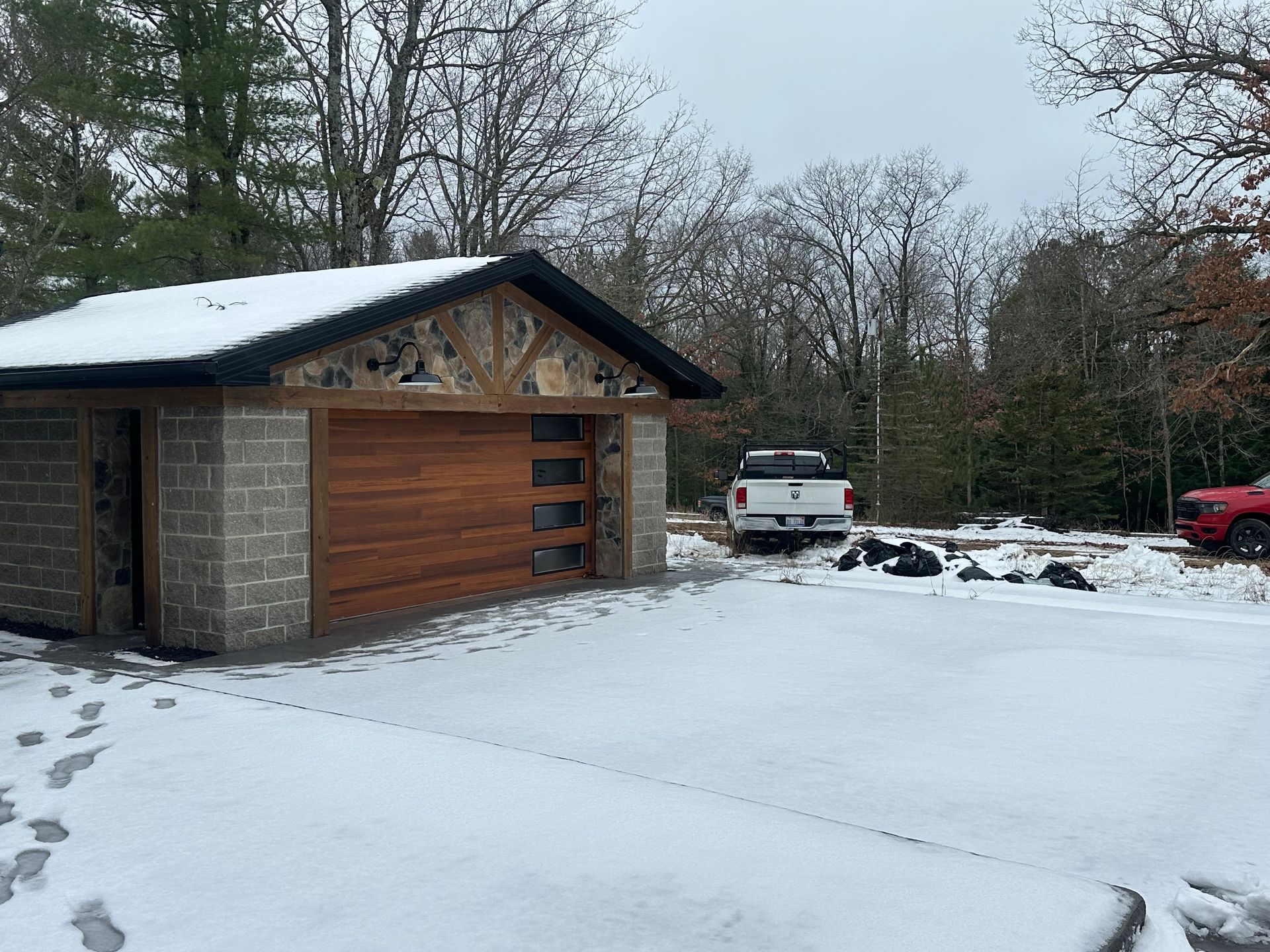 Snowy scene: Garage with wooden door, stone facade, and a pickup truck parked outside.