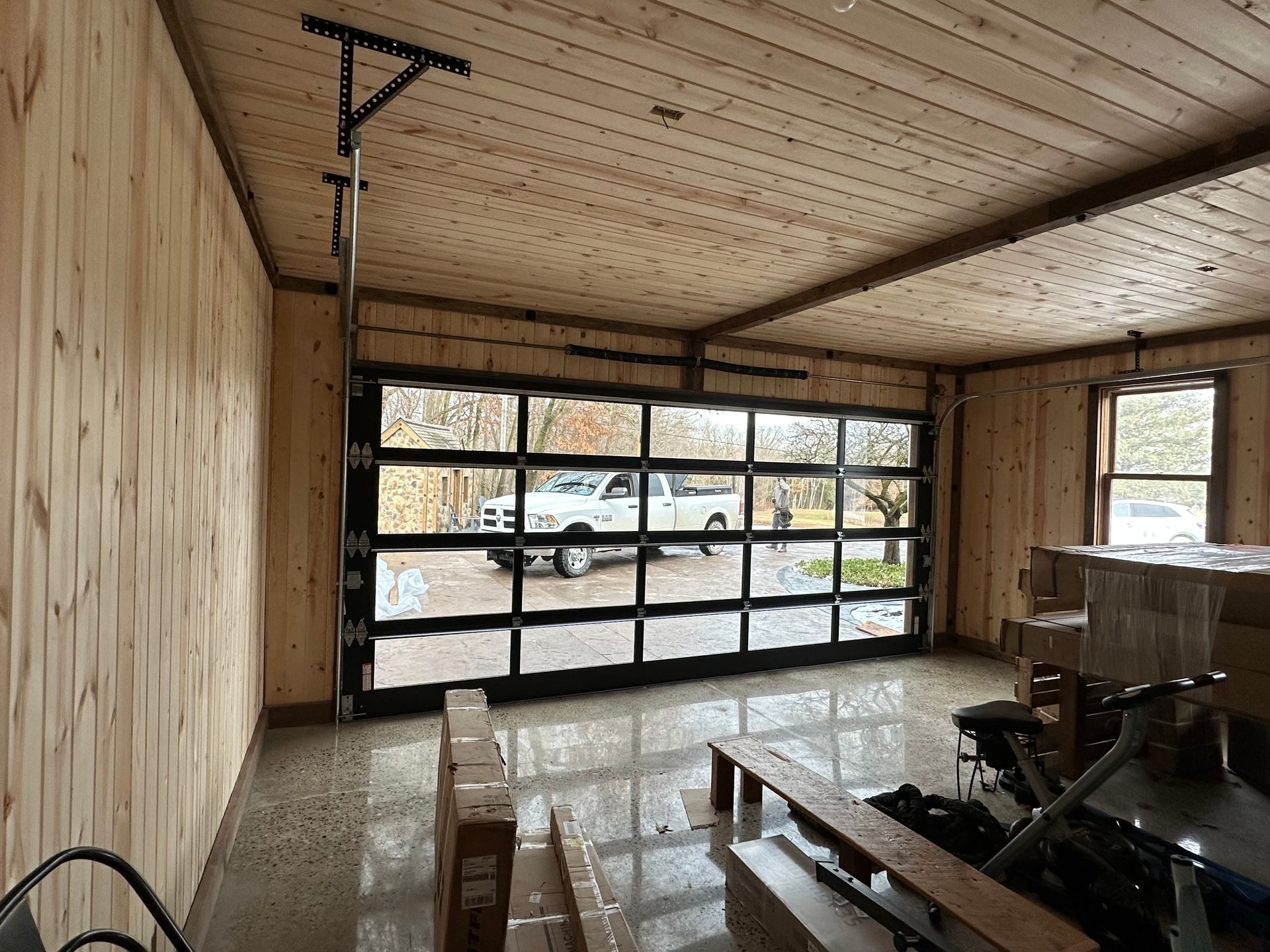 Interior of a modern garage with glass door. Natural wood walls and ceiling, a vehicle is visible outside the door.