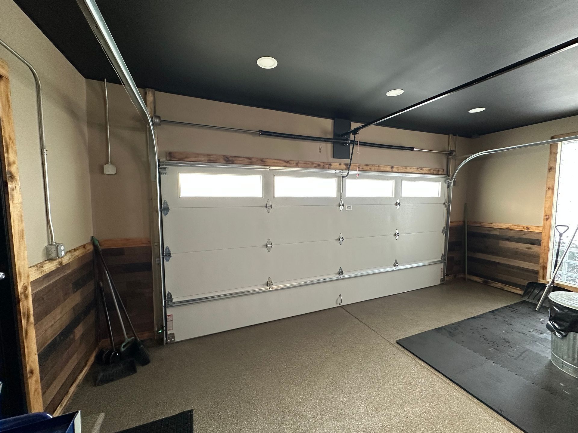 Interior of a garage with a closed white door. Walls have wood paneling and a dark ceiling.