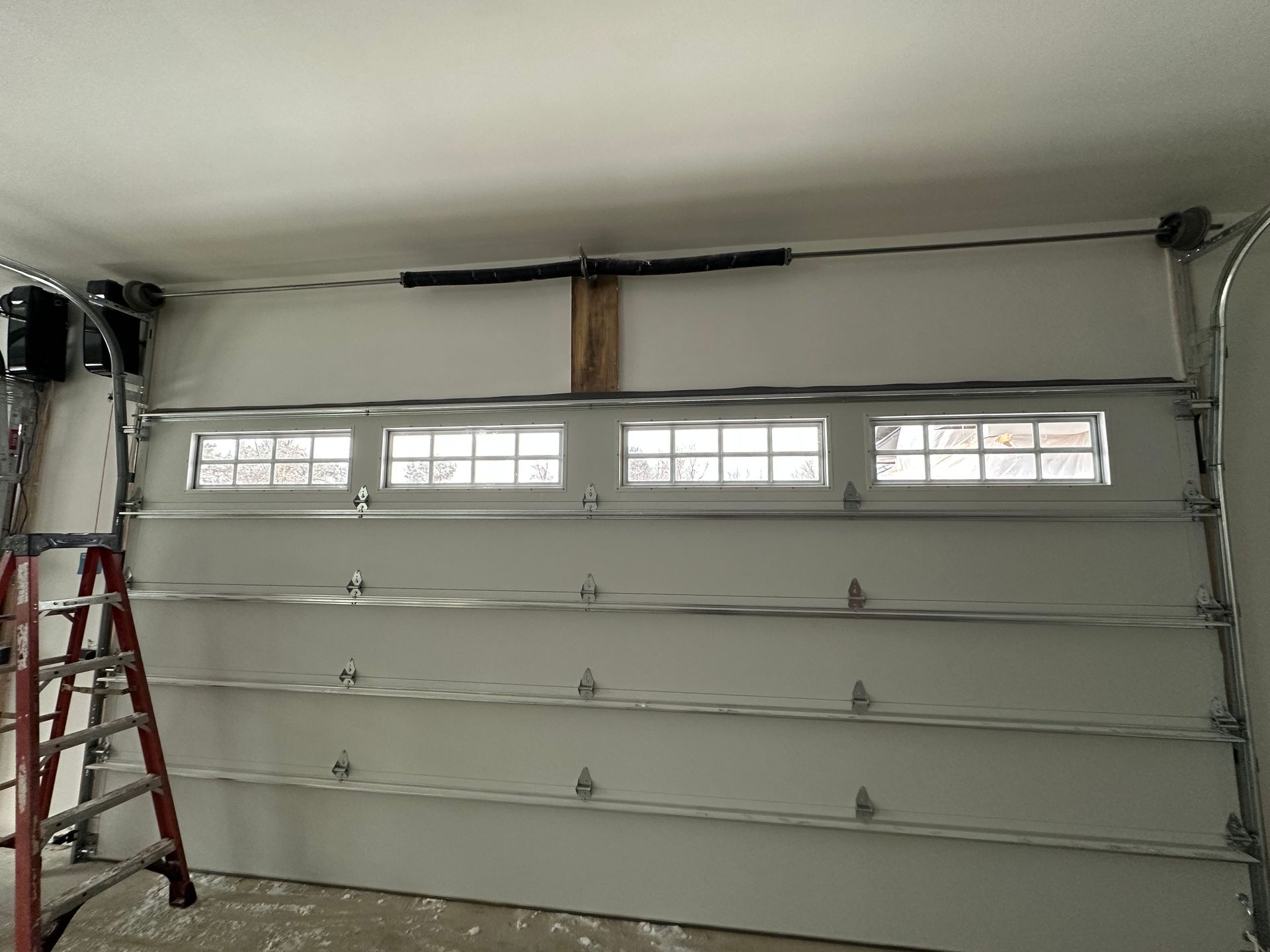 Garage door partially open with windows, a ladder, and a torsion spring.