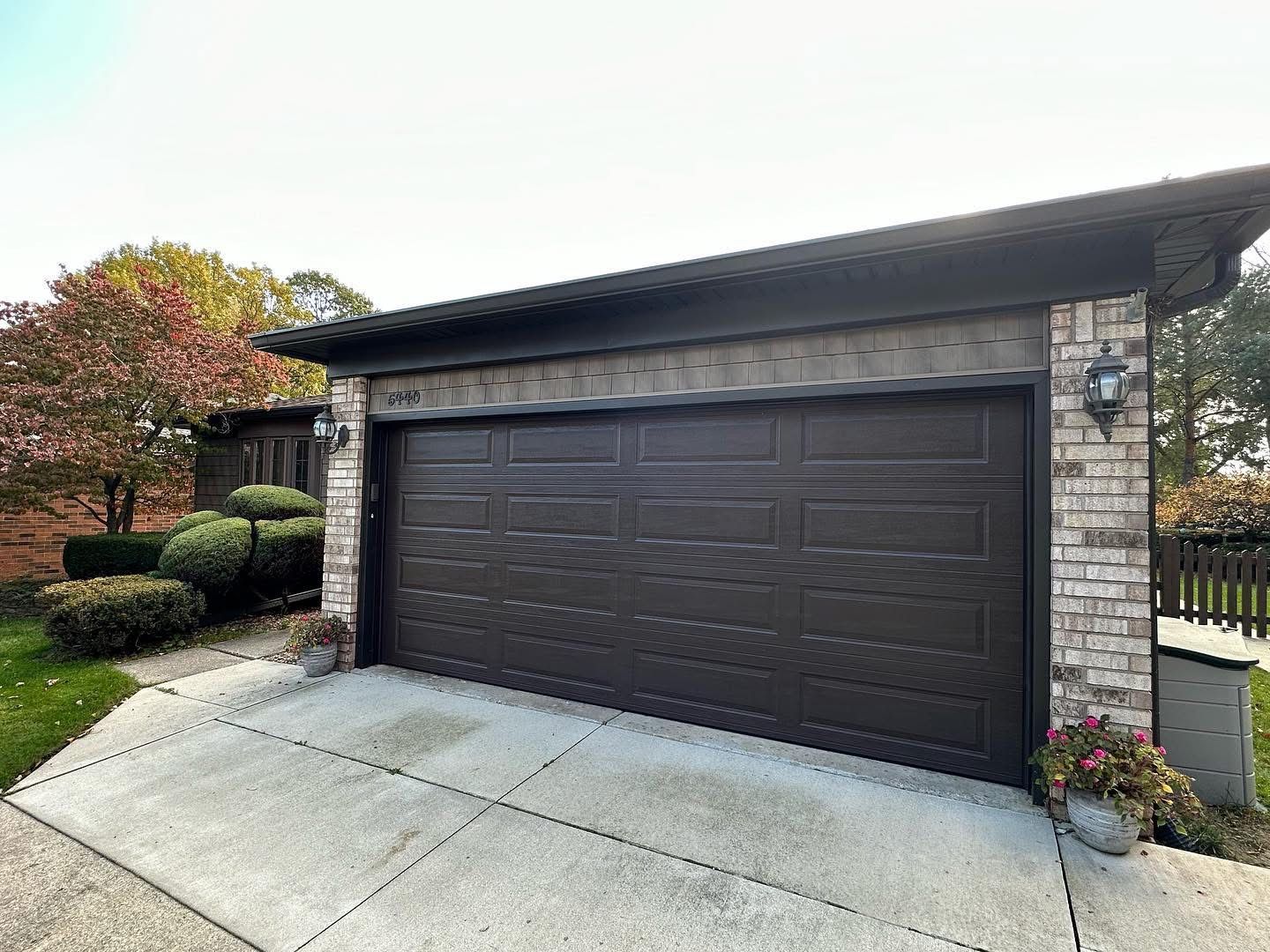 Brown garage door with brick accents on a house. Concrete driveway.