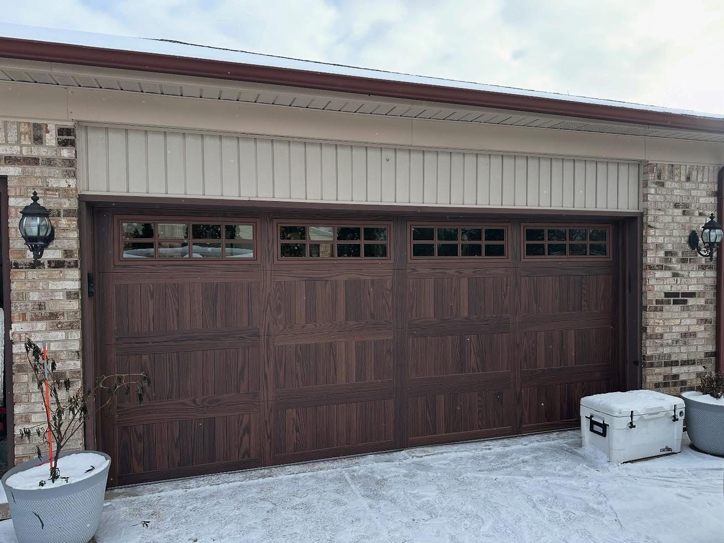 Brown garage door with windows, snow on the ground, brick building.