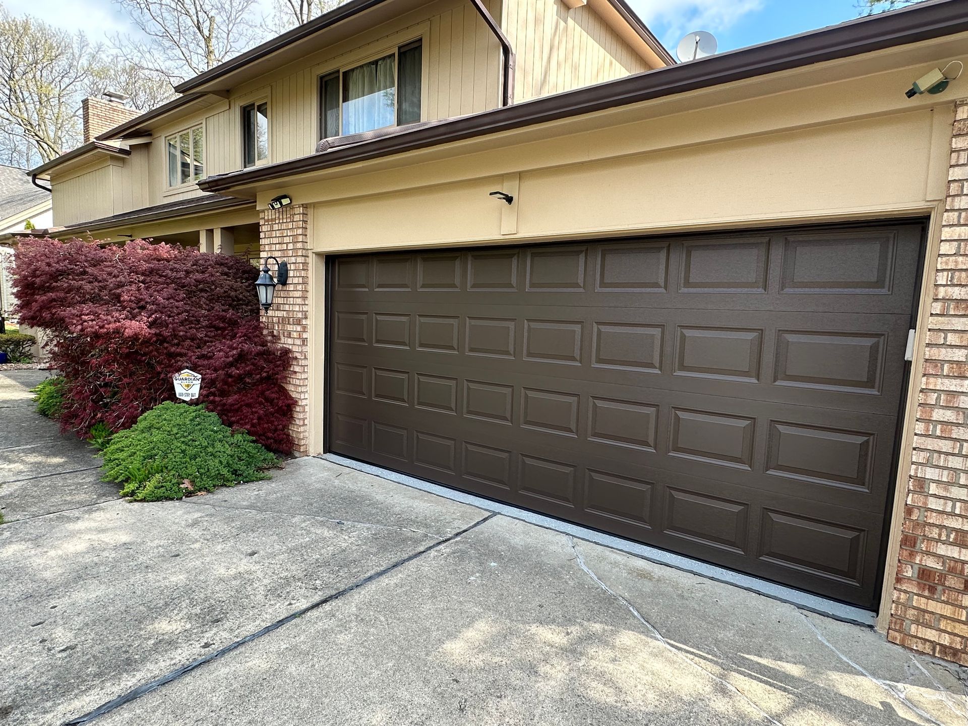 Brown garage door on a tan house with a red bush and concrete driveway.