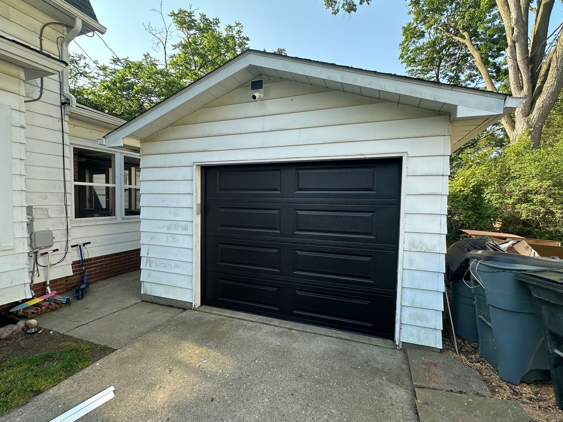 Black garage door on a white building, concrete driveway, and trees.