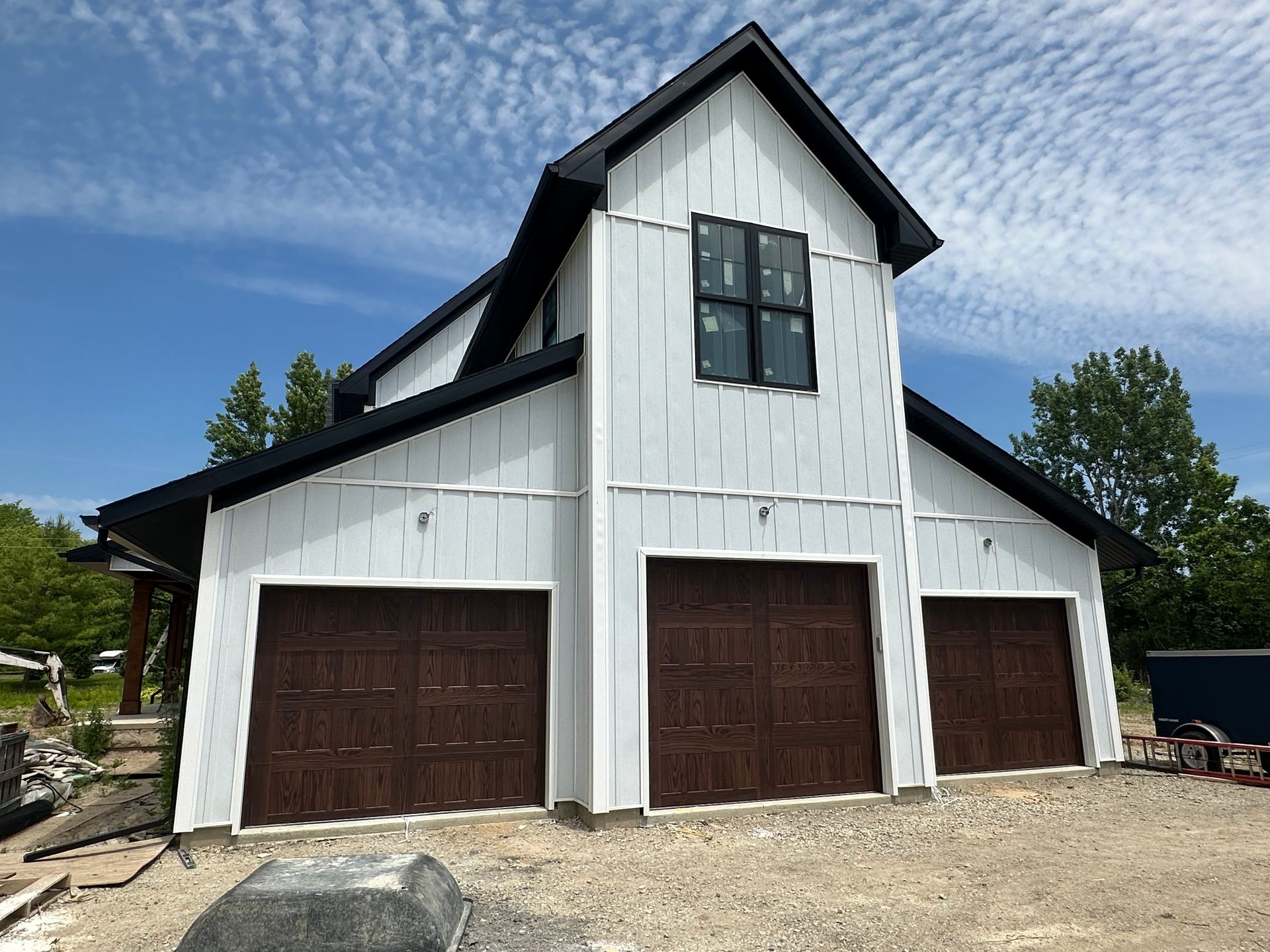 White building with three brown garage doors, black roof trim, and a small square window.
