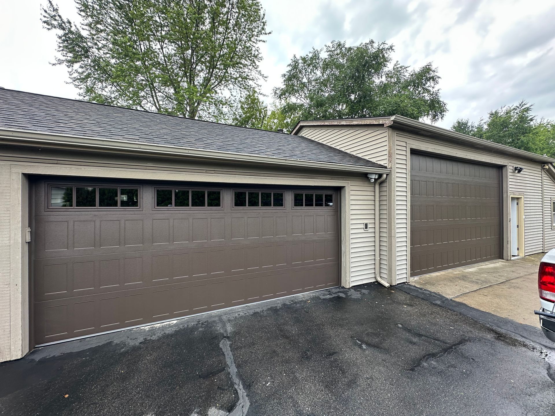 Two brown garage doors on a beige building, asphalt driveway. Overcast sky.