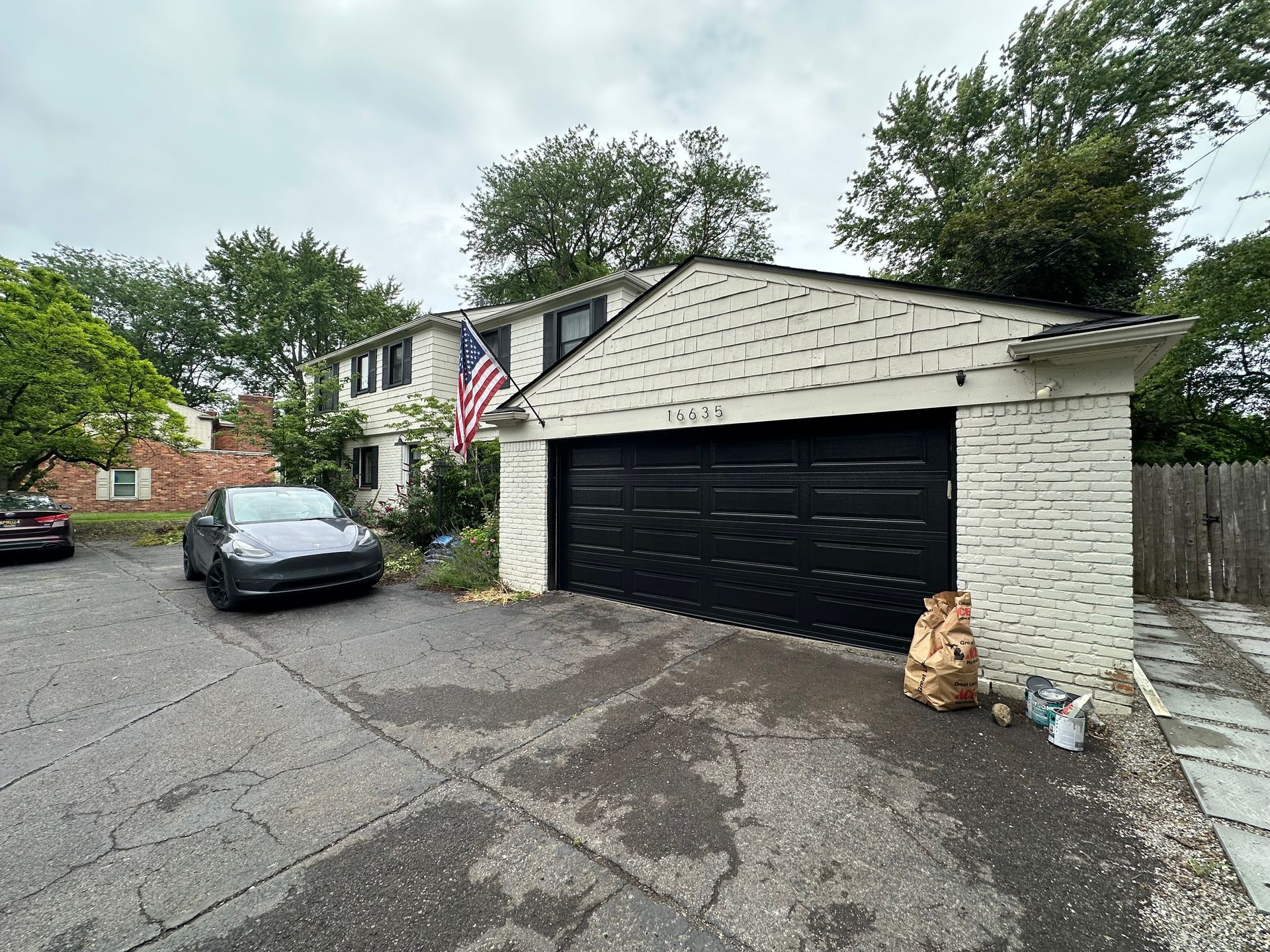 A two-story house with a black garage door and a car parked in the driveway. An American flag flies.