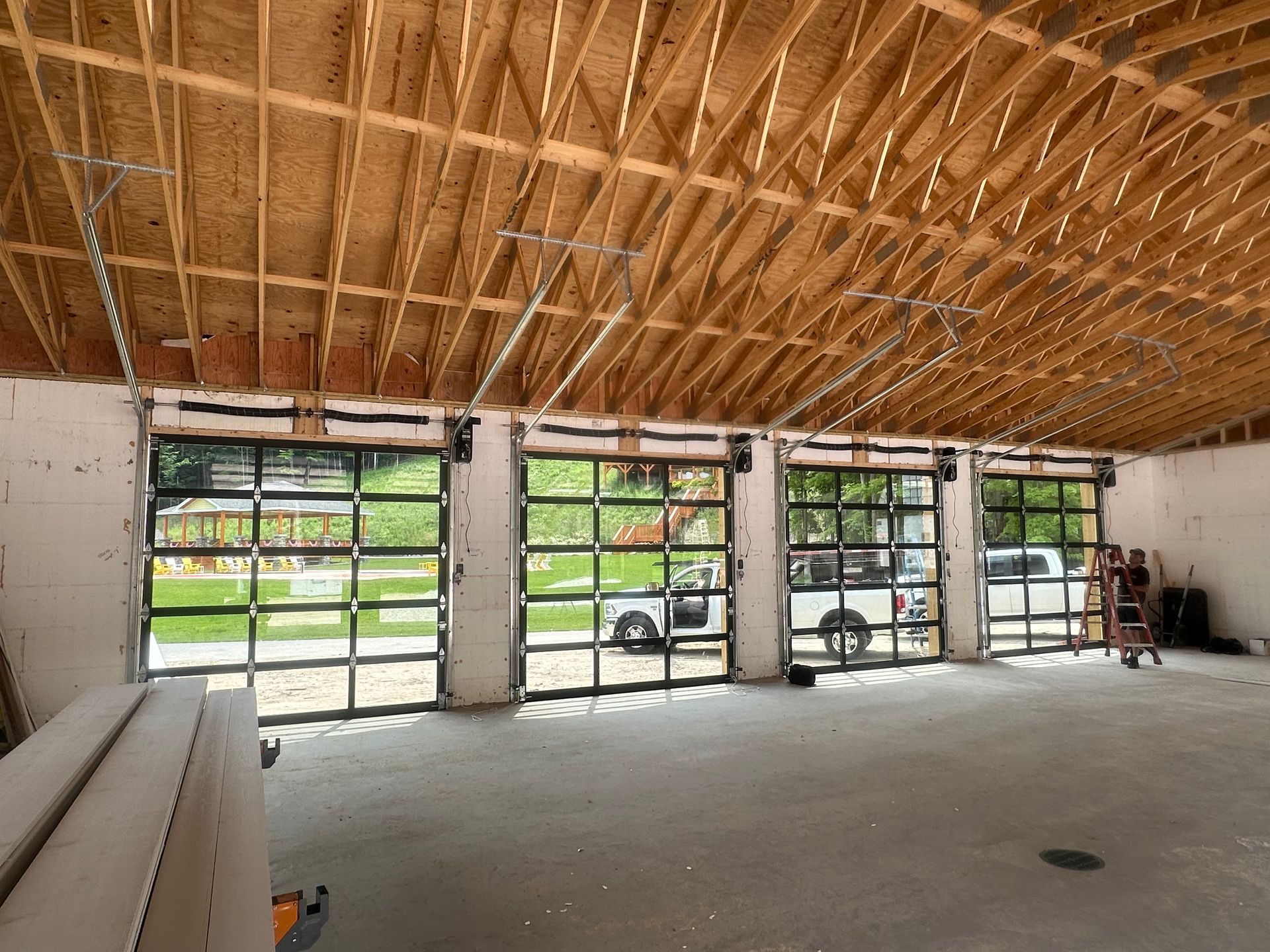 Interior of a building under construction, featuring three glass garage doors. Open ceiling and exposed wooden beams.