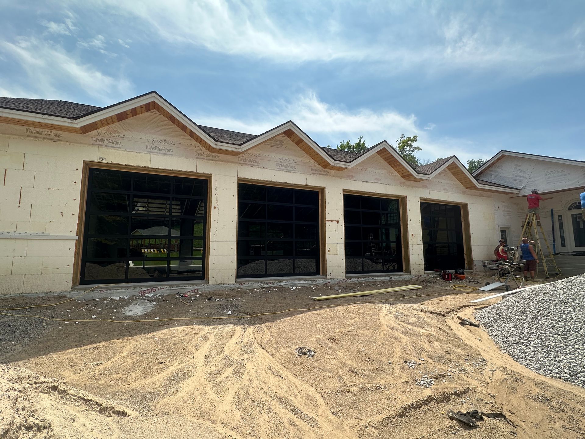 Exterior of a building under construction, featuring garage door frames, brown roofline, blue sky.
