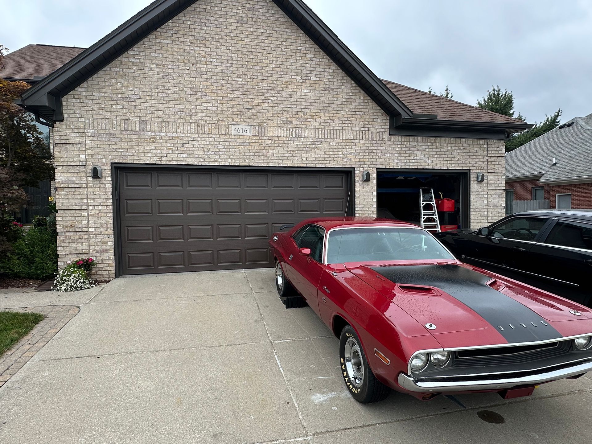 Red classic car parked in front of a brick garage with a brown door.