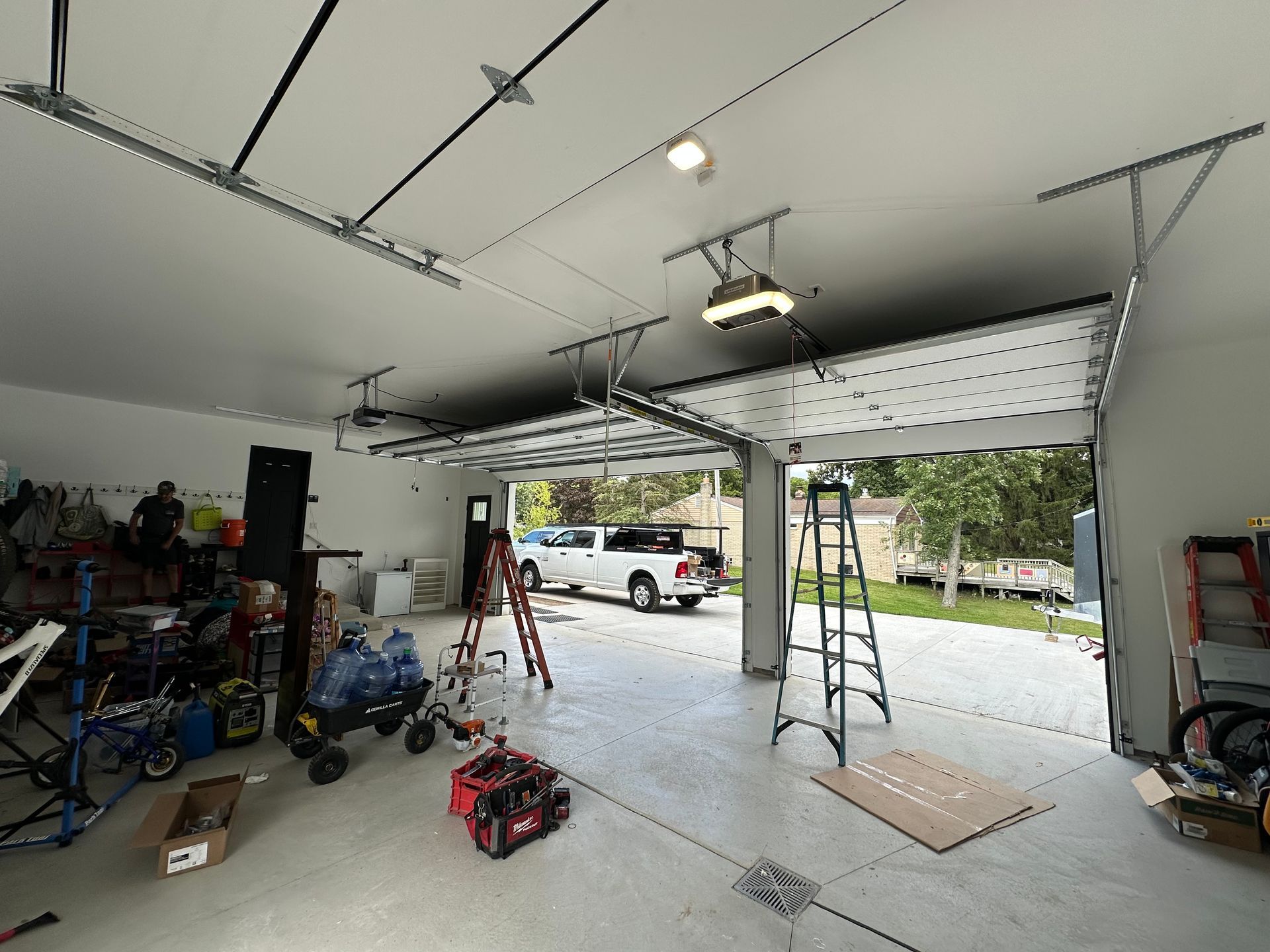 Garage interior with overhead doors, tools, and a truck outside.