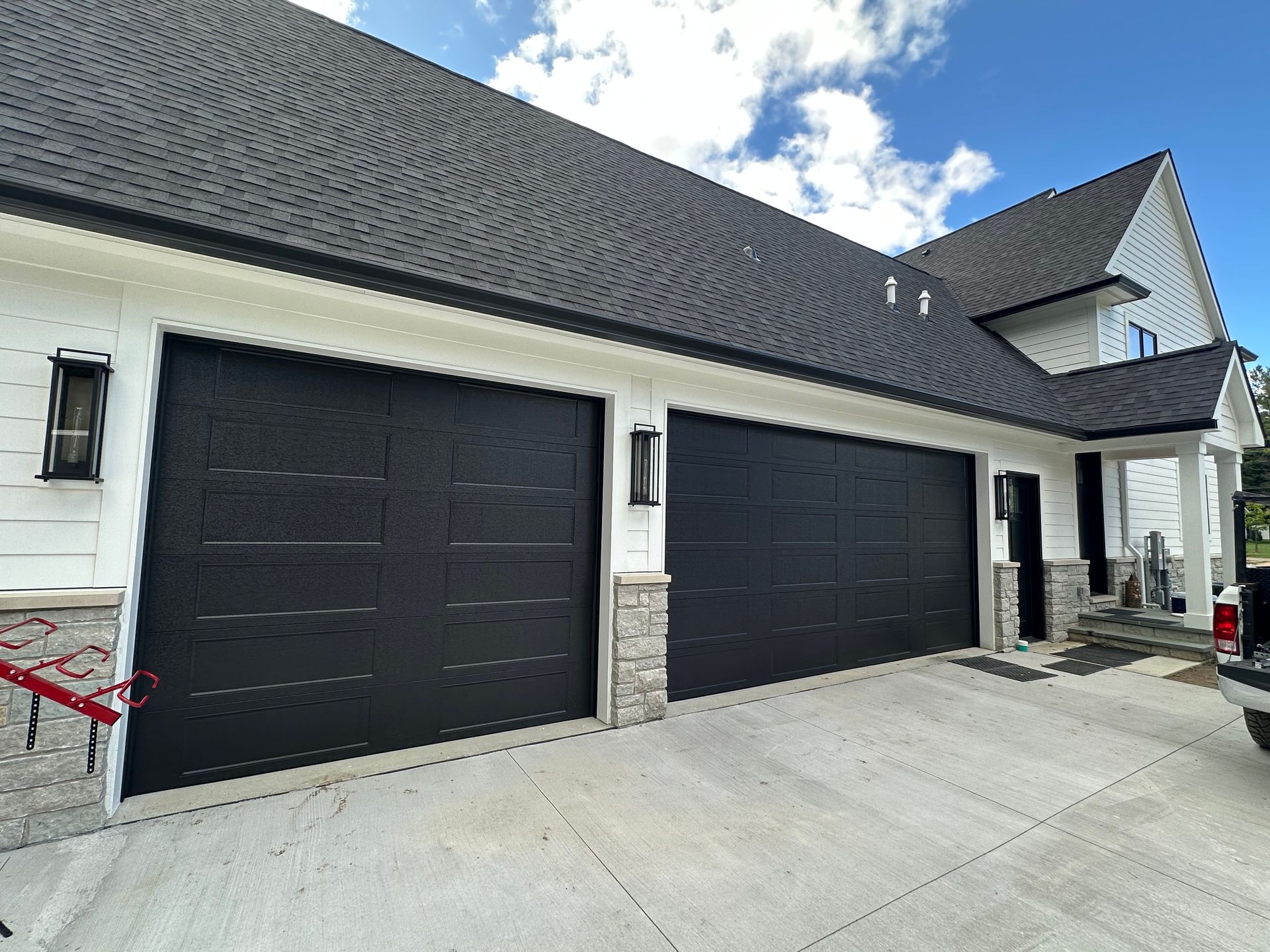 Two black garage doors on a white house with a dark roof. Stone accents. Cloudy sky.