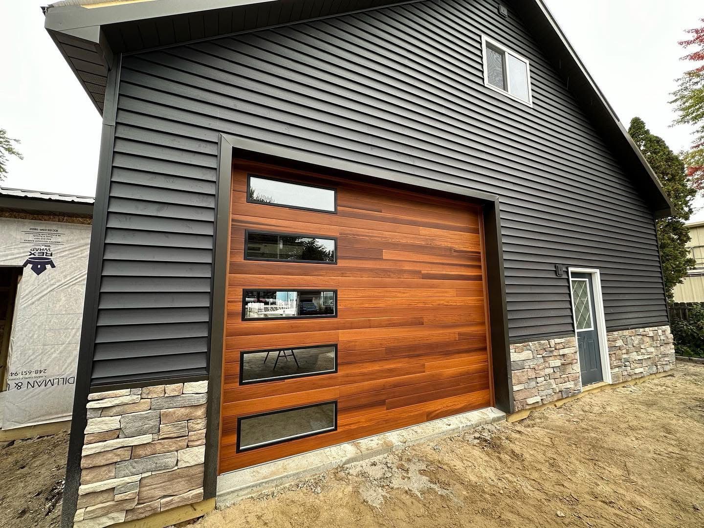Dark gray modern garage with wooden door and stone accents.