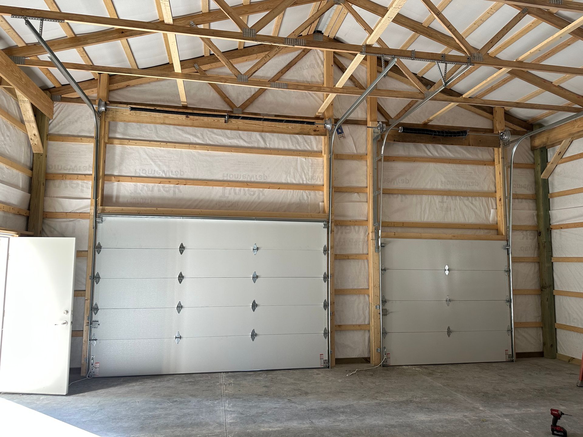 Two white garage doors inside a wooden framed building under construction.