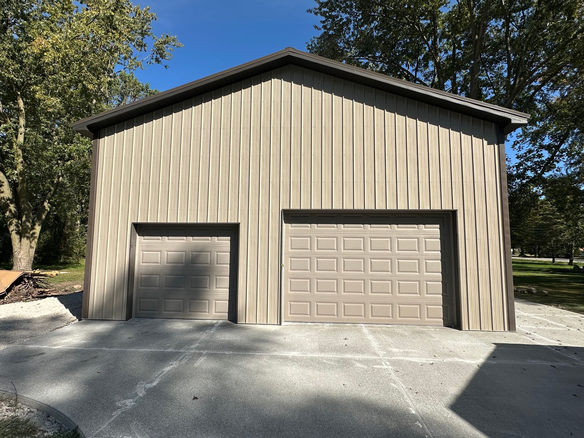 Tan metal garage with two doors and textured siding, set on a concrete driveway.