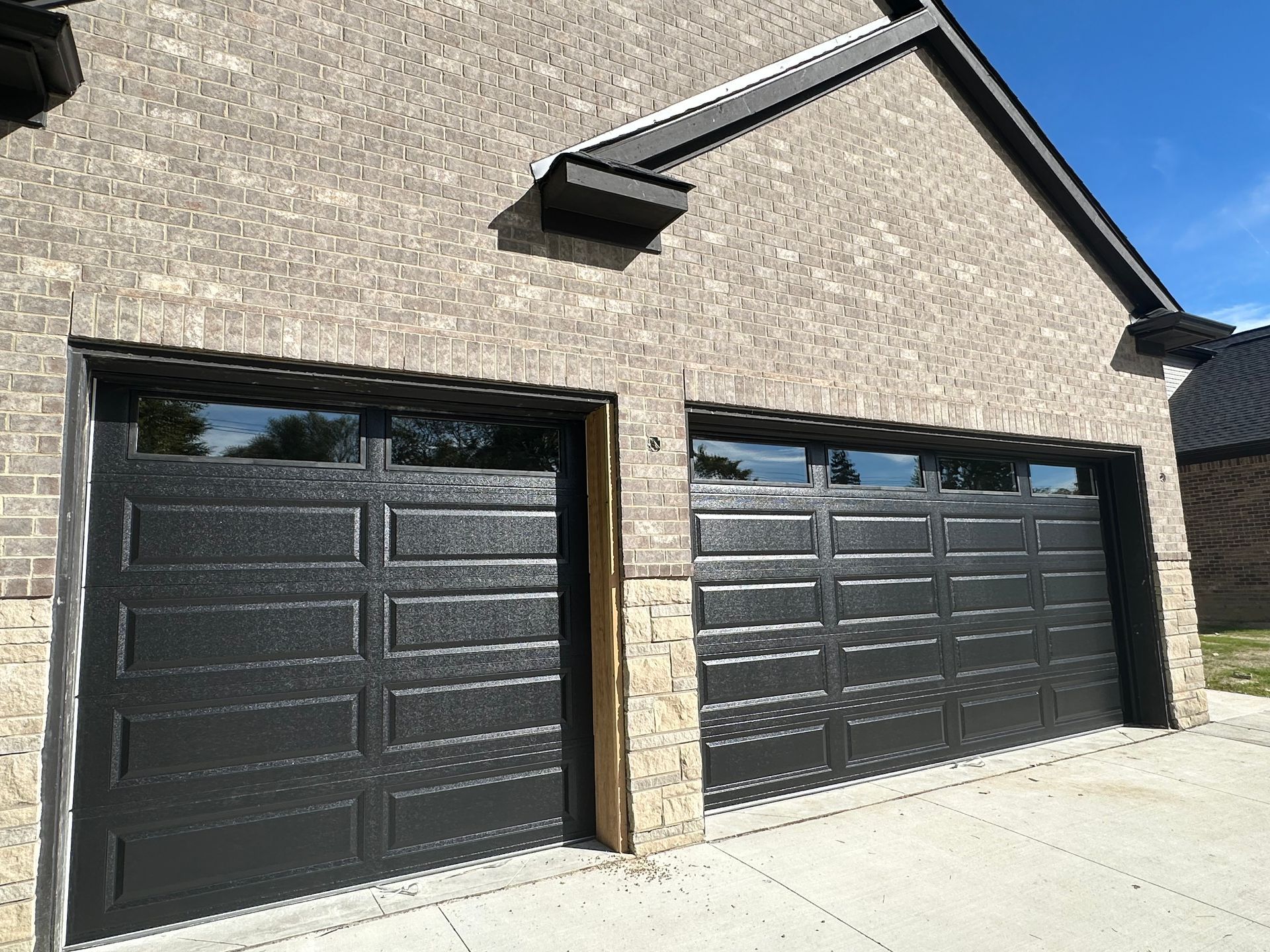 Two black garage doors with windows, set in a light brick building.