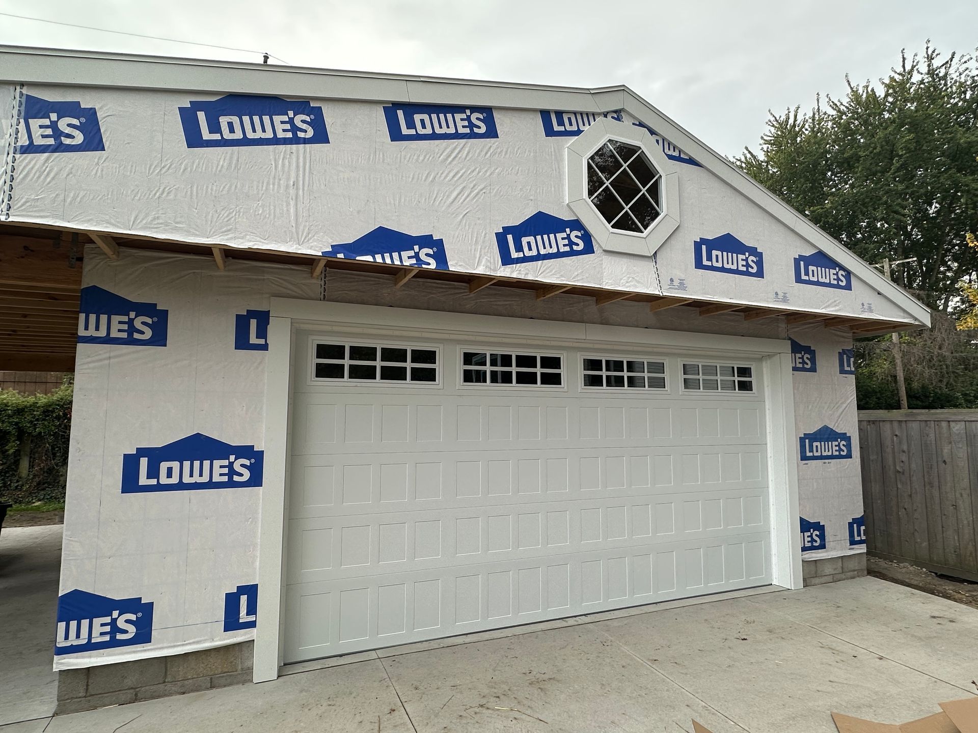 White garage door on a new construction garage with Lowe's wrap. Octagon window at the roof peak.