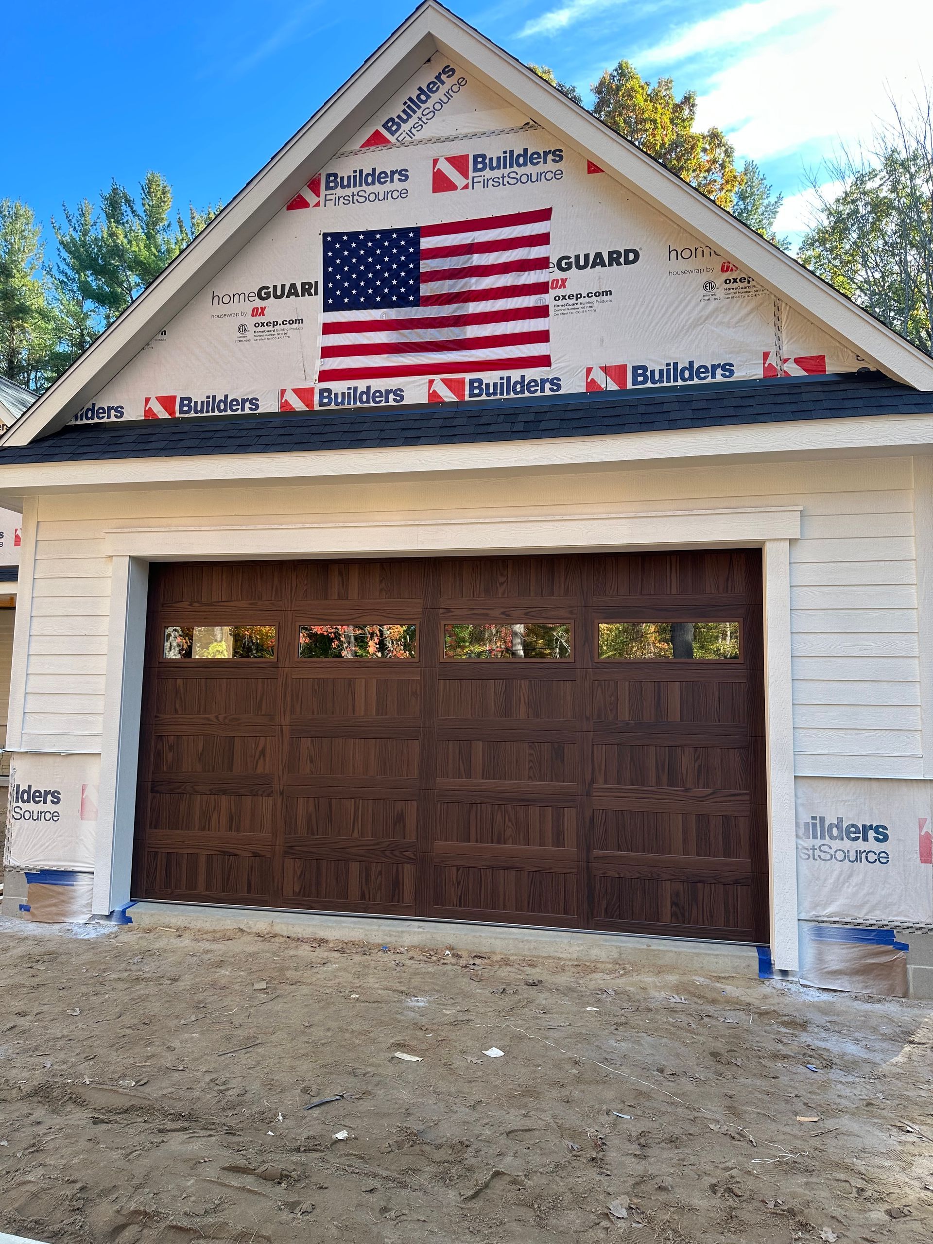 Garage with a brown door, American flag in the gable, and white siding.