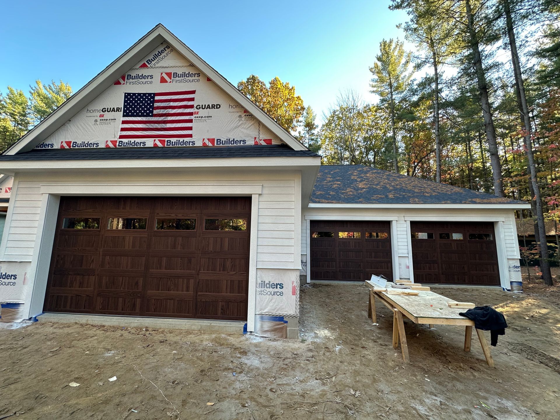 New residential garage with brown doors, American flag on the gable, and surrounding trees.