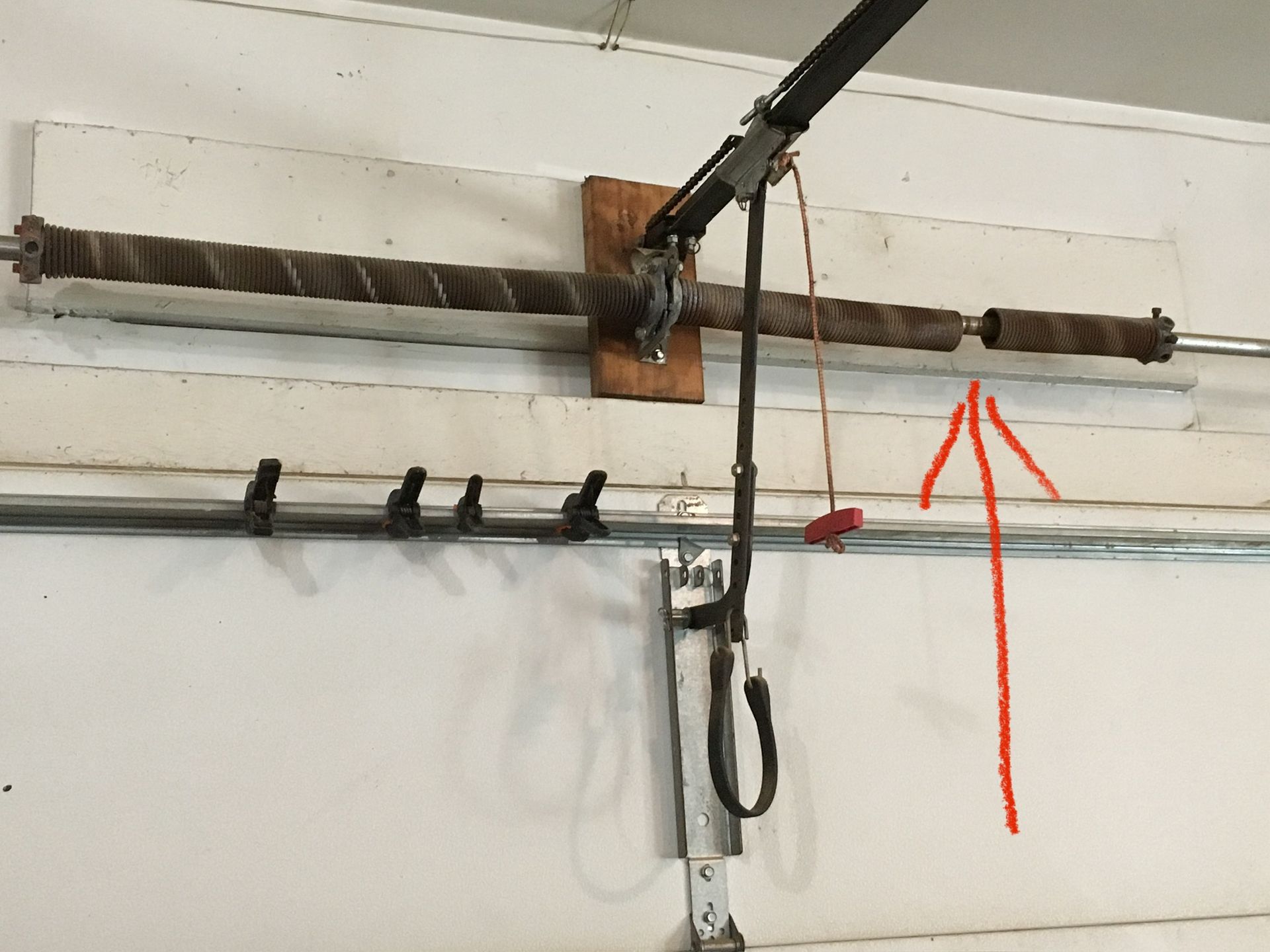 Garage door torsion spring, with red arrow pointing to one end of the spring.