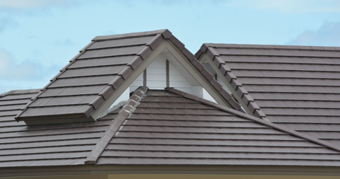 Brown shingled roof with a triangle-shaped dormer against a cloudy sky.