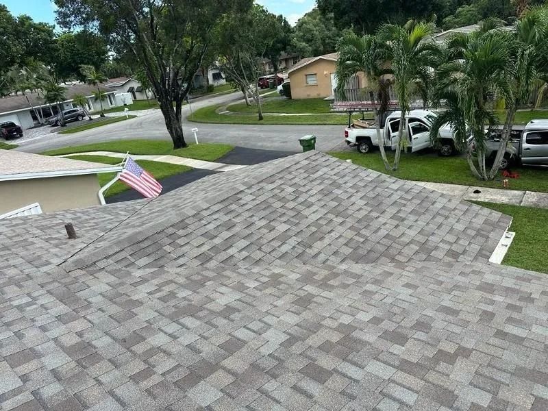 Overhead view of a house with a new multi-tone shingle roof. Vehicles and American flag are in the yard.
