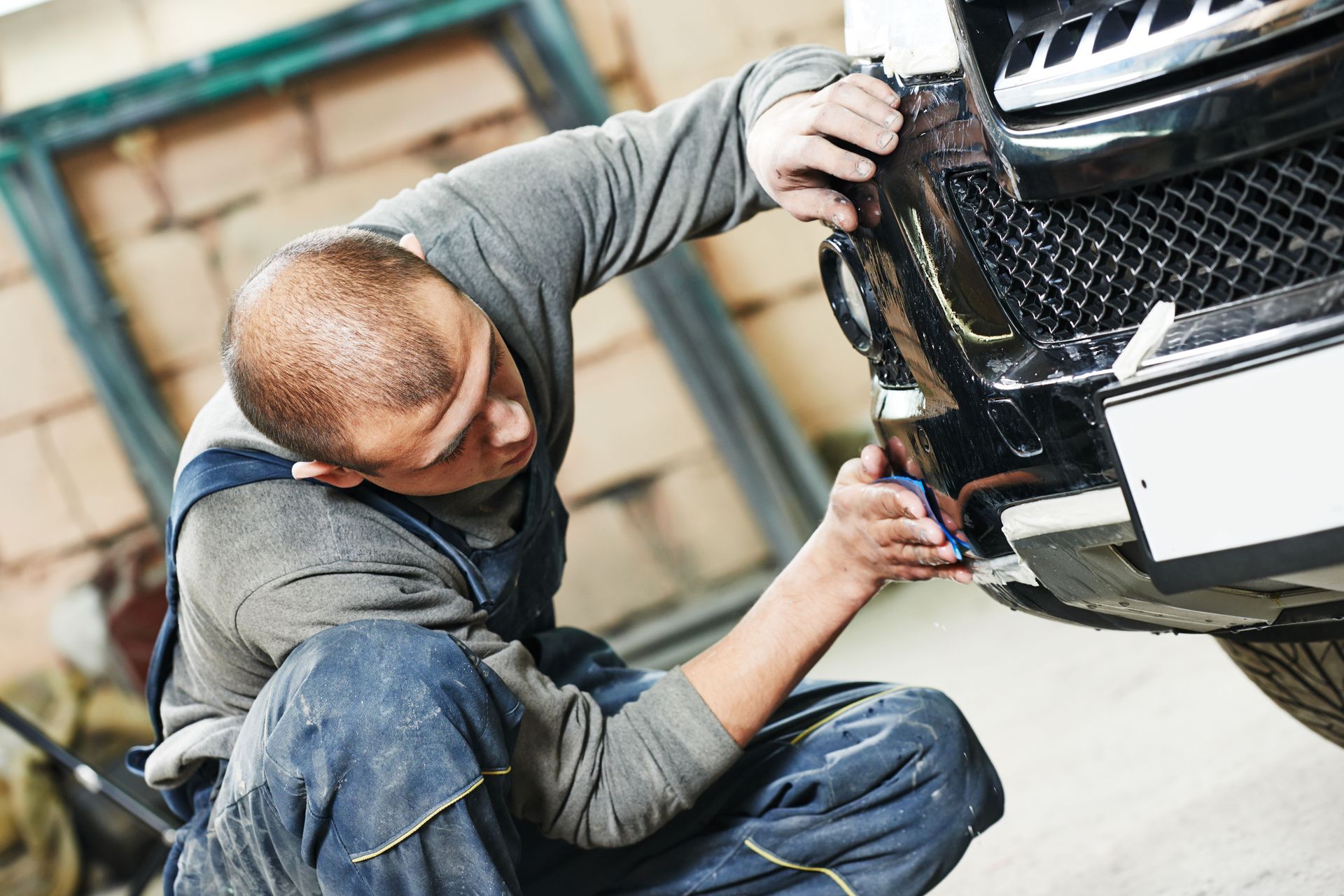 Mechanic inspecting a black car bumper in a workshop.
