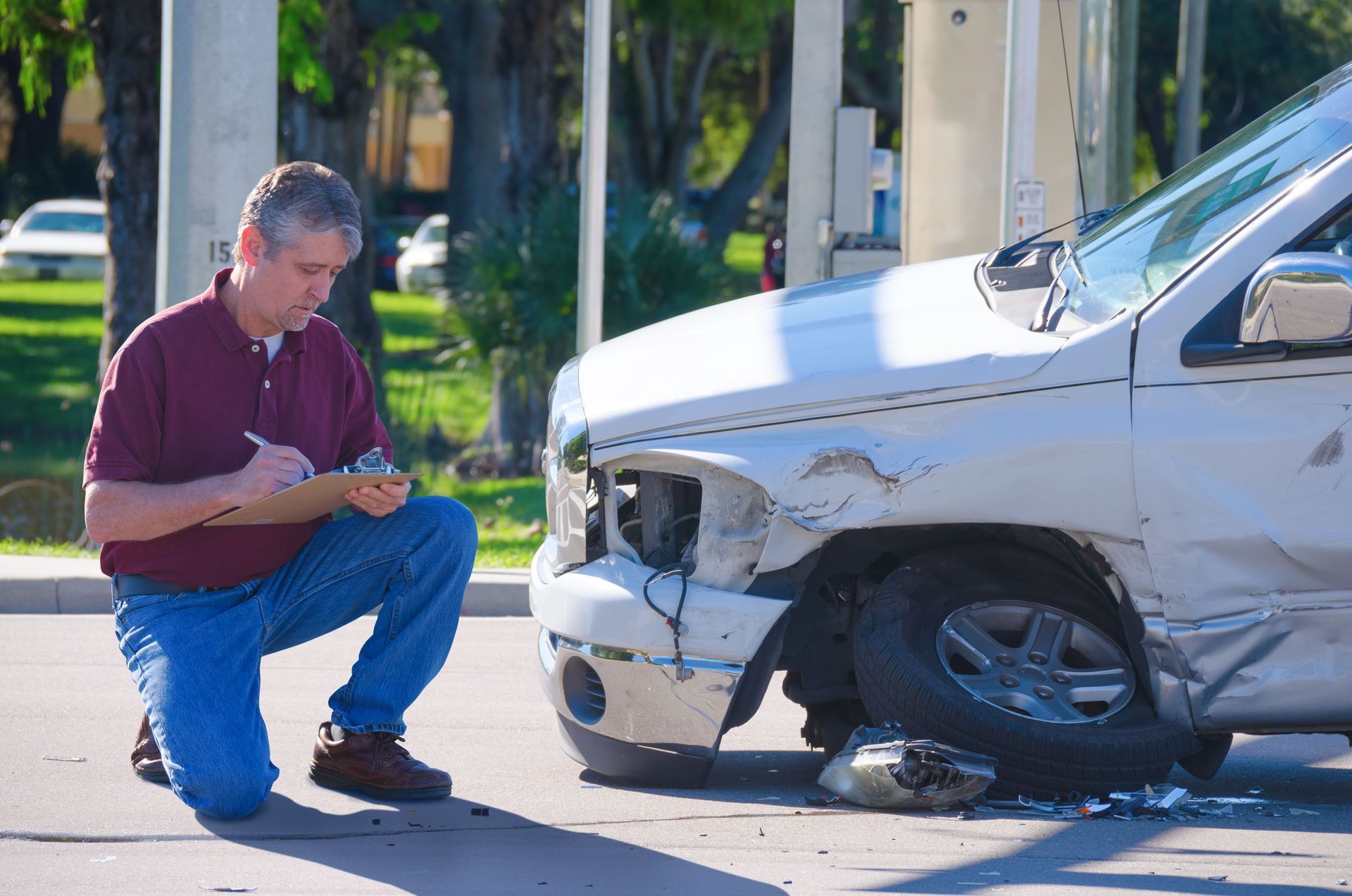 Man assessing damage to a white truck after a collision; writing on a clipboard.