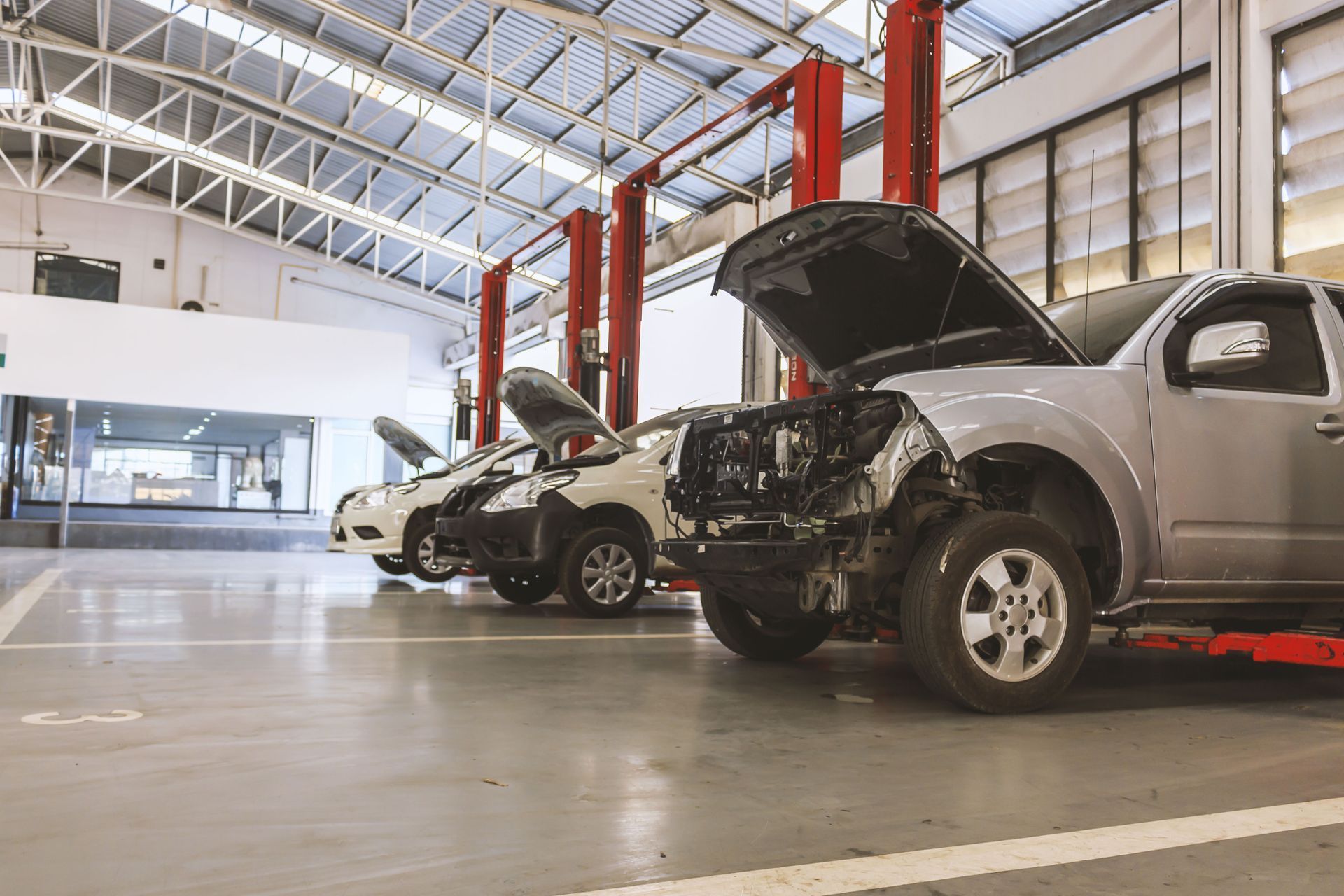Cars with open hoods inside a garage with red lifts and a concrete floor.