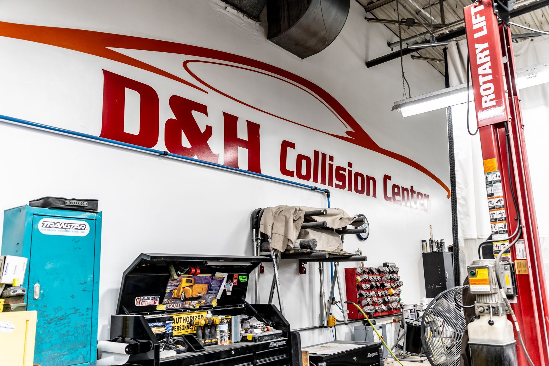D&H Collision Center interior with logo, toolboxes, and a red car lift.